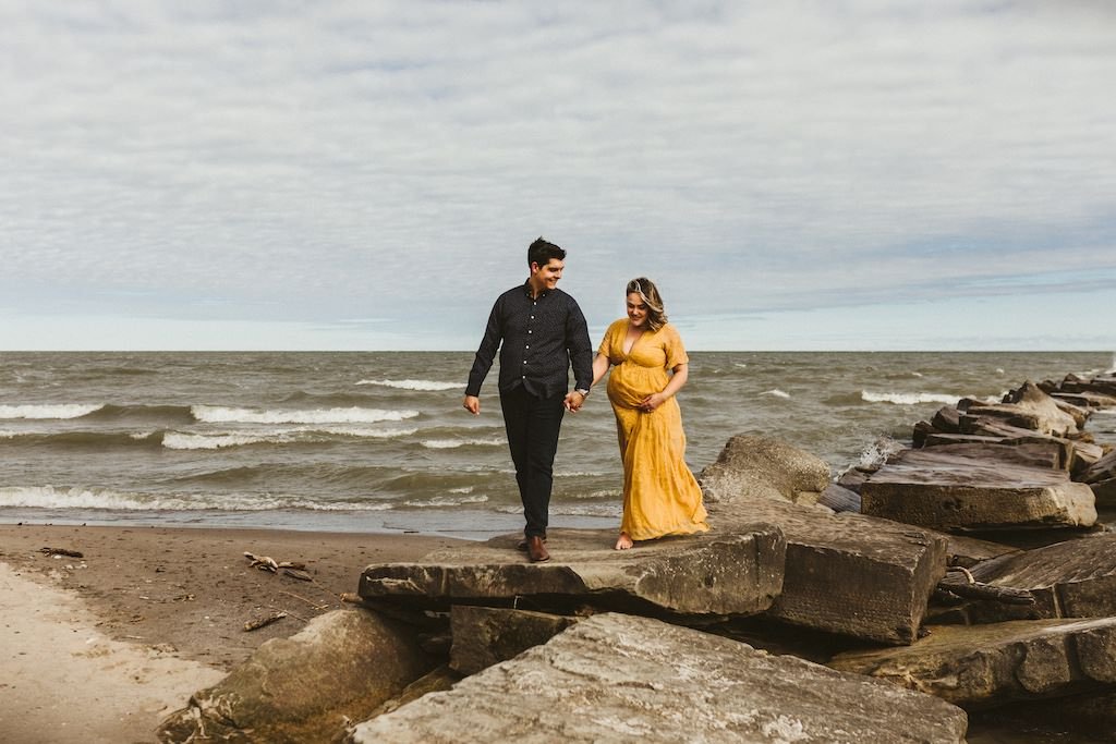 A couple walking on rocks near Huntington Beach, Ohio during a maternity session. 