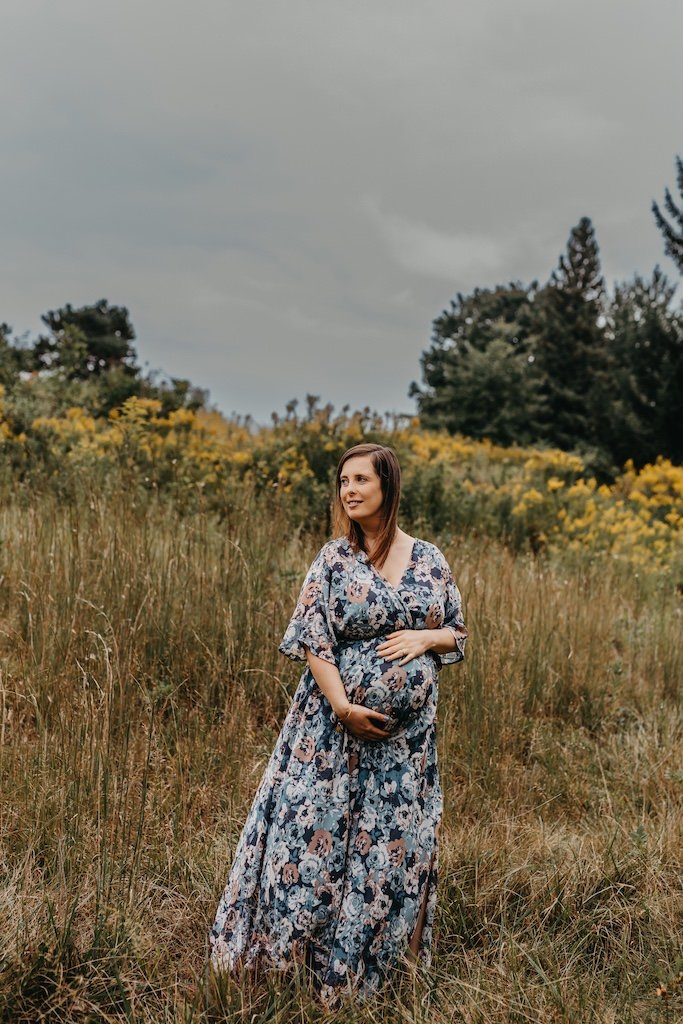 Portrait of pregnant woman in floral dress amongst tall grass in Cleveland, Ohio.