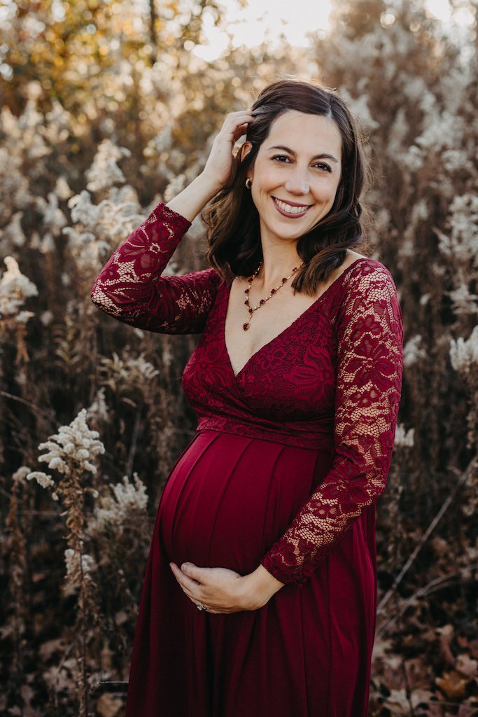 Pregnant woman wearing a red gown with lace sleeves posing for maternity photography. 