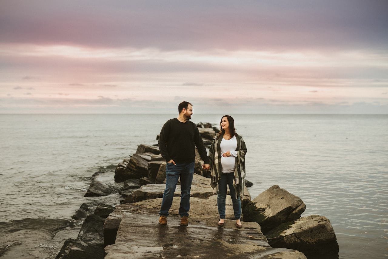 Parents to be posing on rocks in Huntington Beach of Bay Village for maternity photoshoot. 