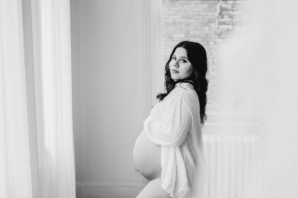 Black and white modern maternity portrait of pregnant woman wearing white unbuttoned shirt in photo studio. 