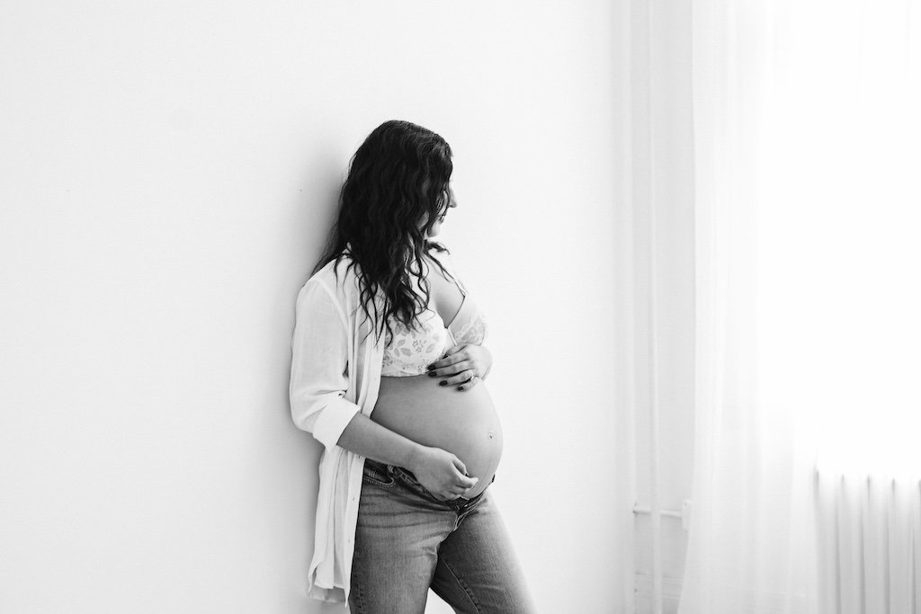 Minimalist black and white portrait of maternity shoot of woman standing near a window. 