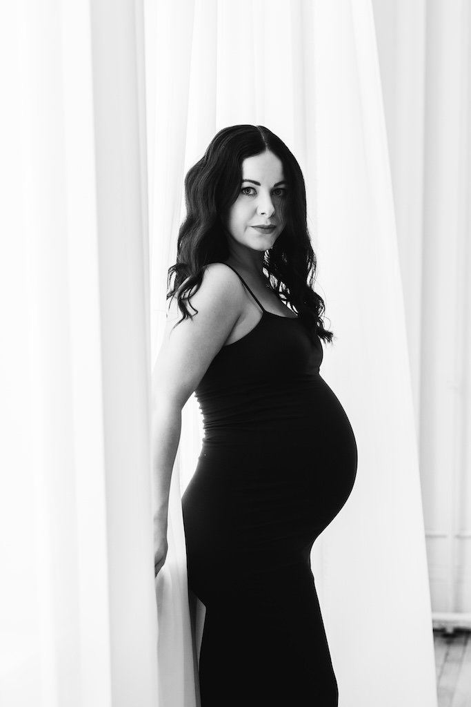 Woman in a black fitted maternity dress posing for pregnancy portraits.