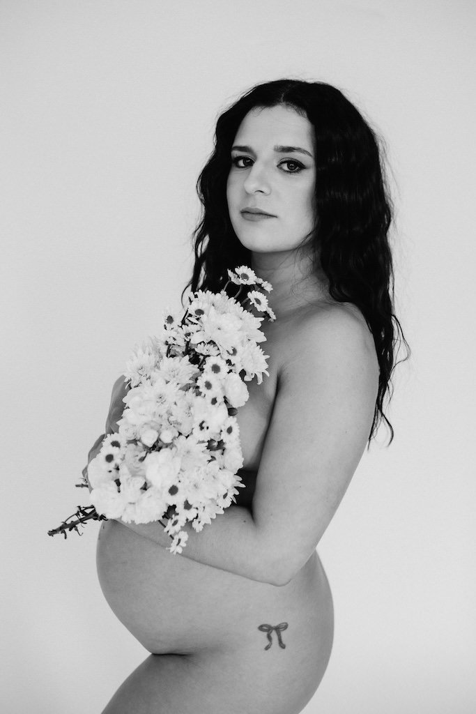 Pregnant woman holding bouquet of flowers over her breasts and pregnant belly in photography studio of Cleveland, OH. 