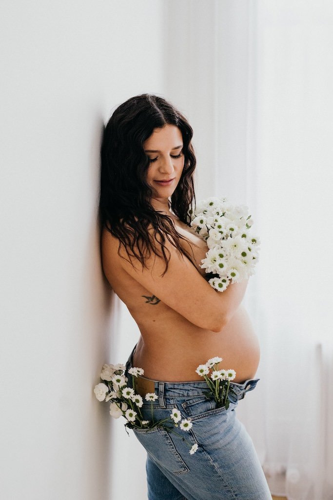 Pregnant woman holding bouquet of flowers during a studio maternity shoot. 