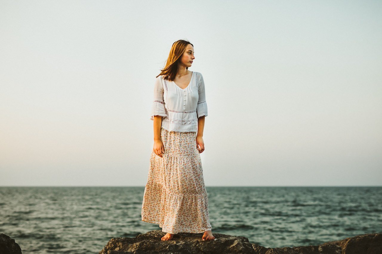 A high school girl posing for senior pictures on rock by Lake Erie in Cleveland, Ohio.