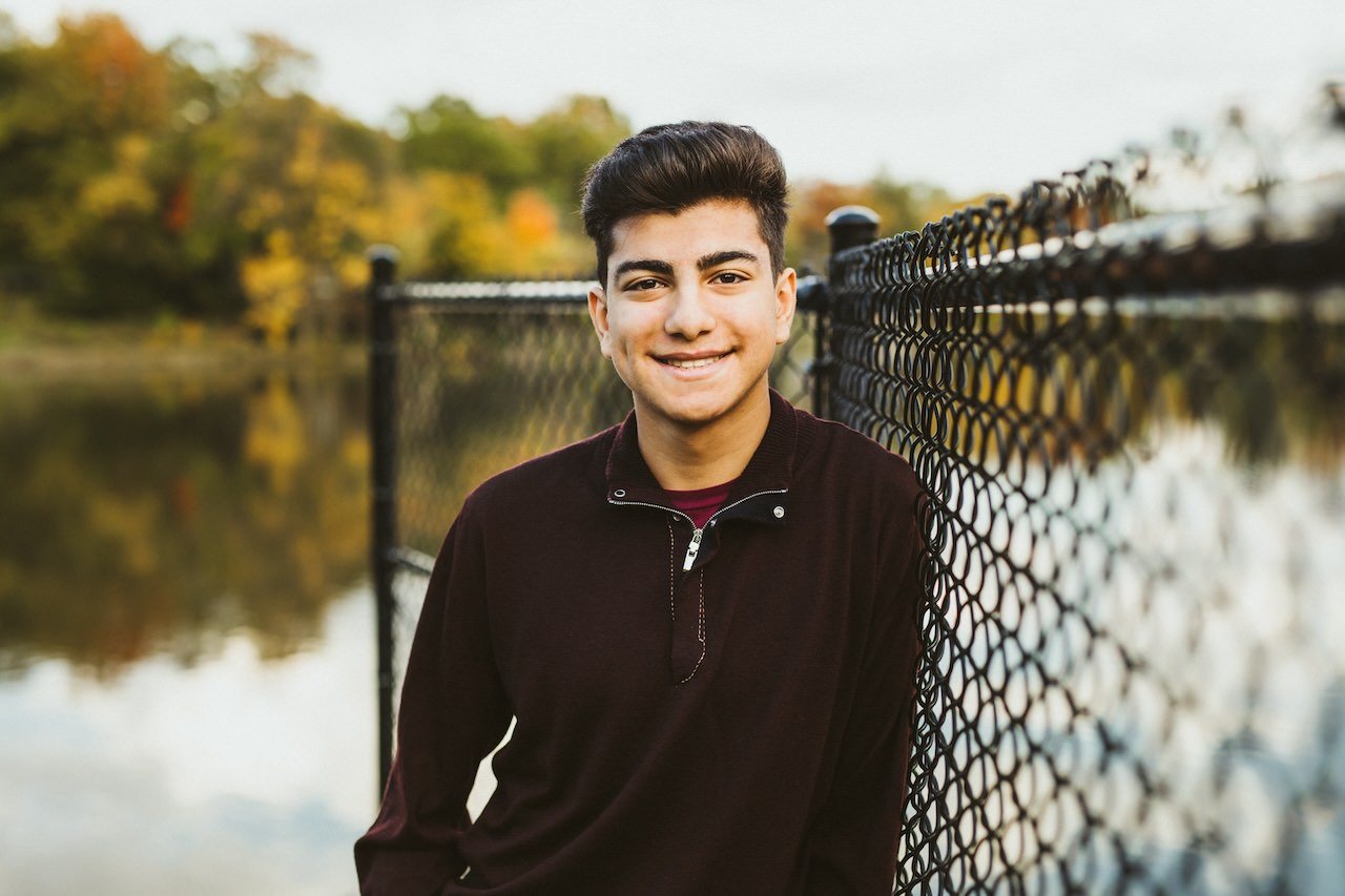 A high school senior boy posing for pictures in fall setting  by a lake in Shaker Heights. 