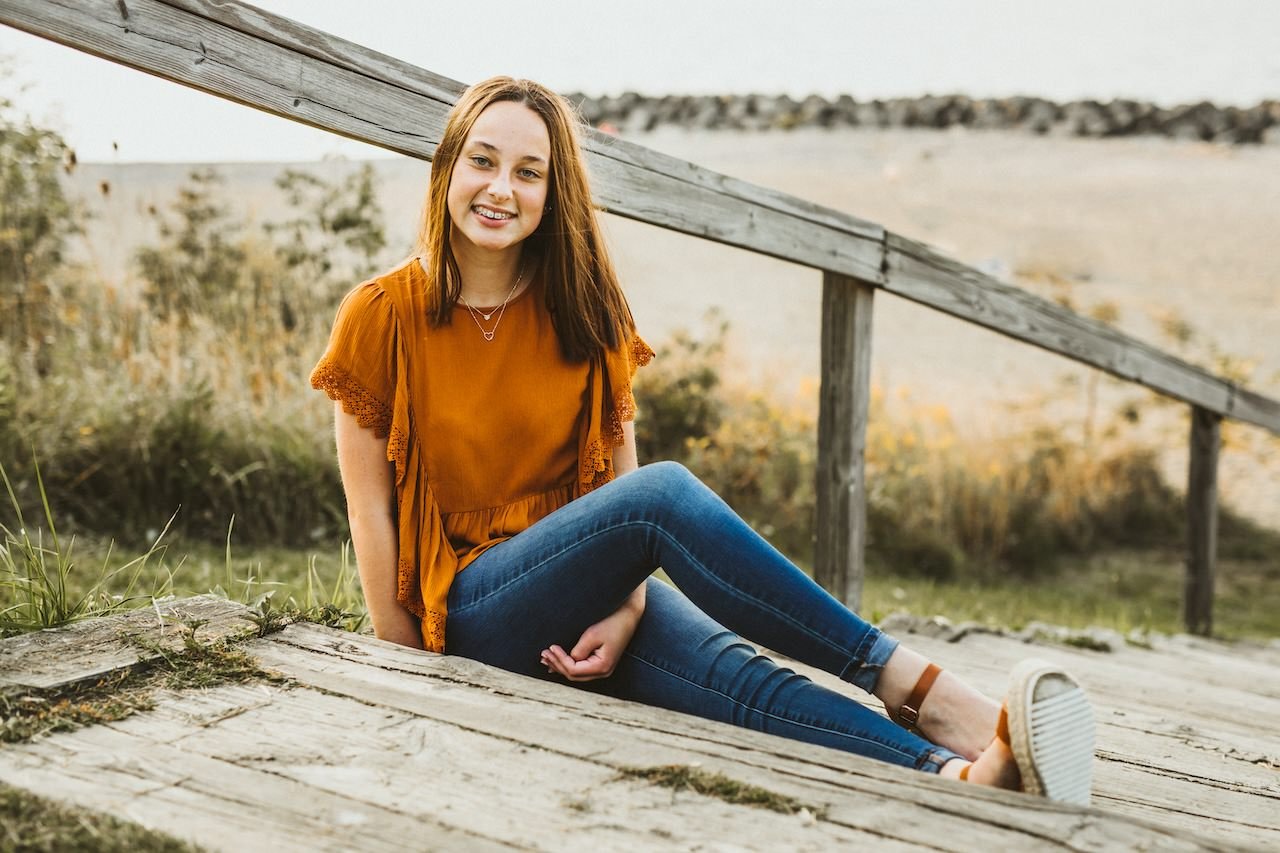 Girl sitting on wooden stairs near a Cleveland beach for senior portraits. 