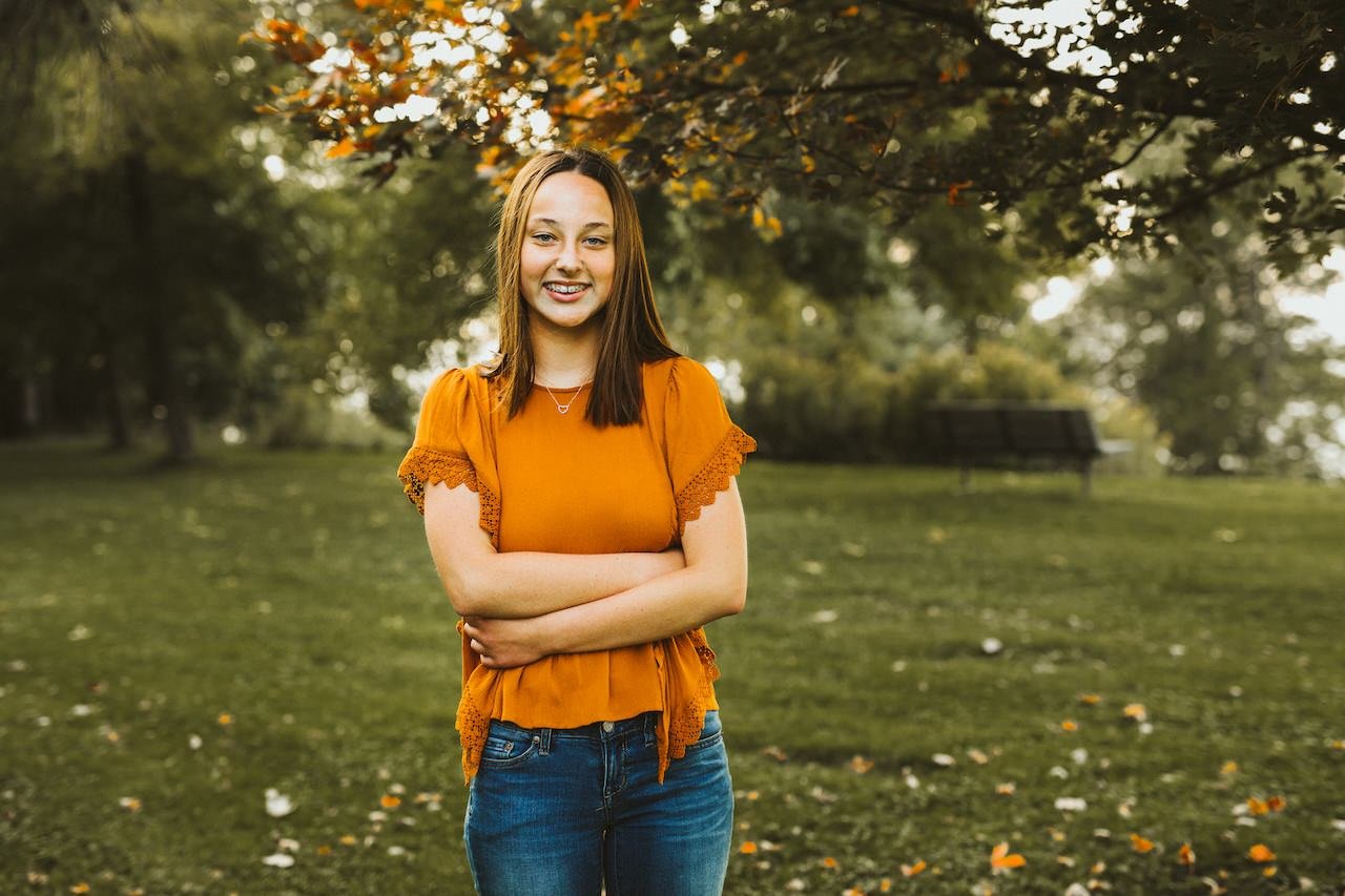 A girl with braces and orange shirt posing for senior pictures in Cleveland. 