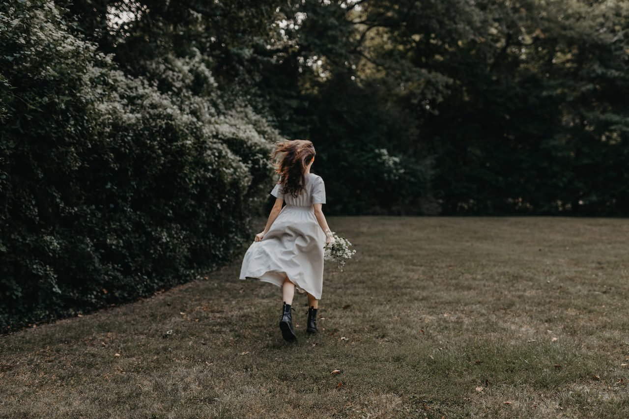 A teenager girl running in the park with long hair during a senior photo shoot. 
