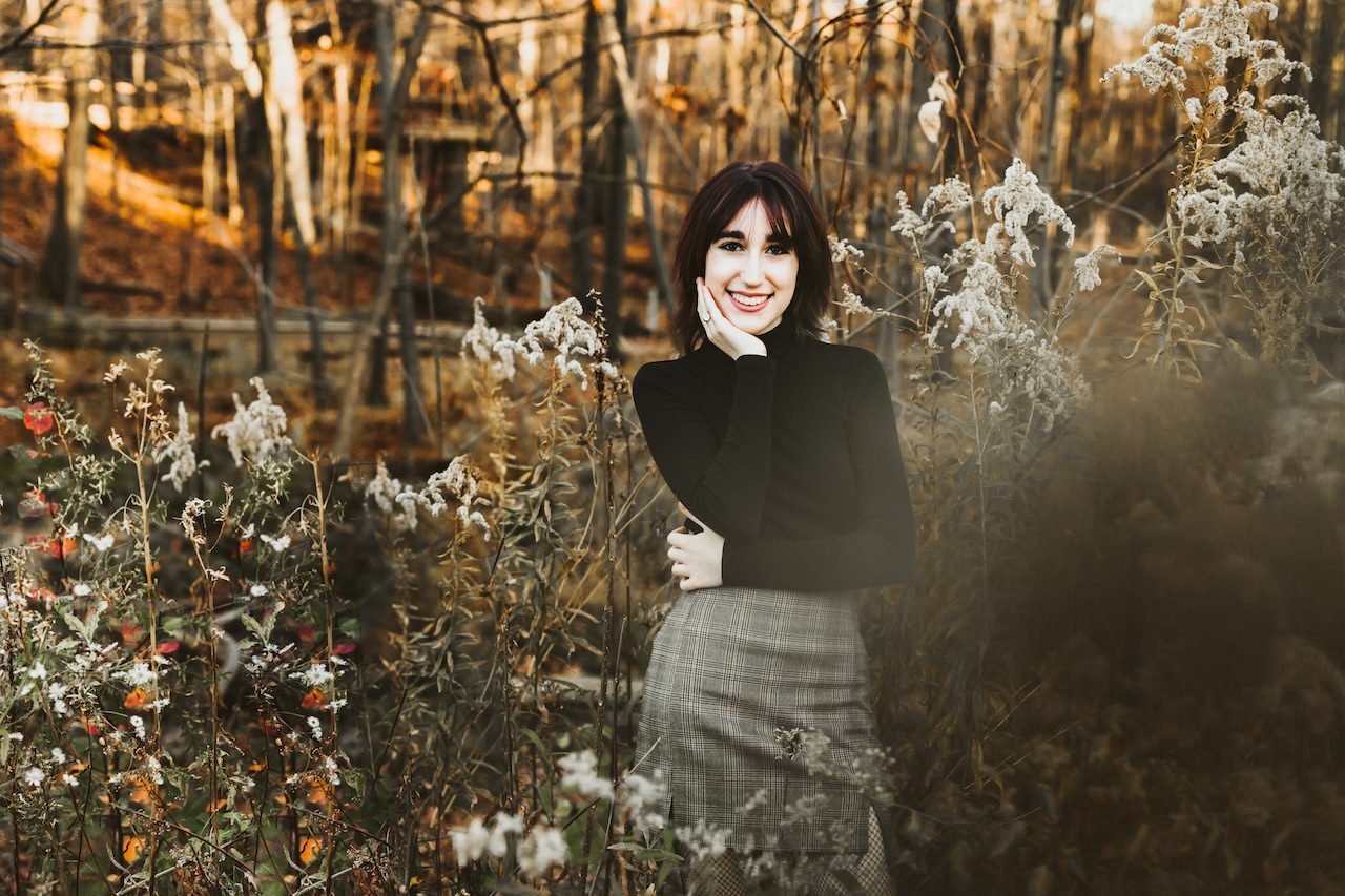A young woman posing for senior photograph in the late fall season outside. 