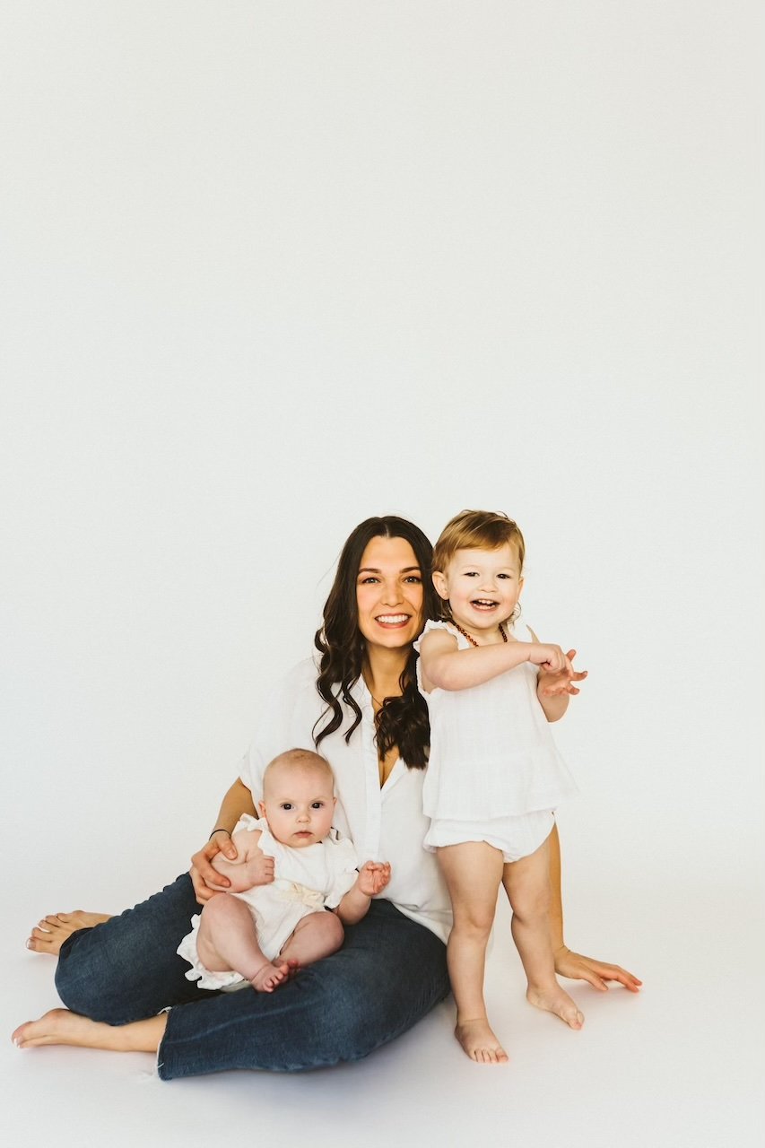A white backdrop photo with mom and two children dressed in white and denim. 