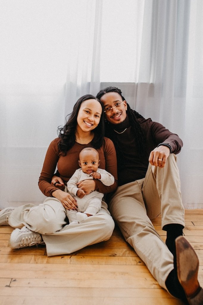 Family of three sitting on wooden floors in a photography studio.