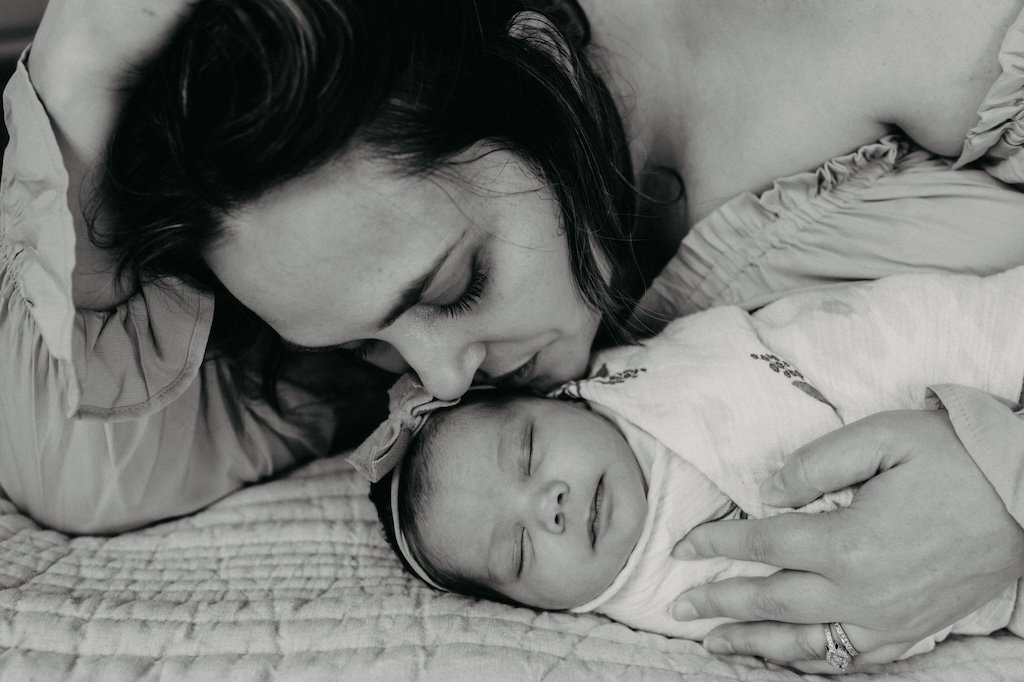 Mom kissing newborn daughter in photo studio.