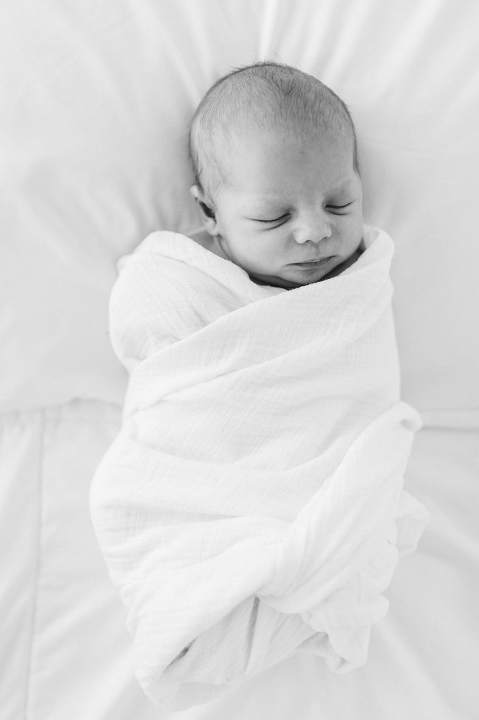 Newborn boy wrapped in white swaddle. 