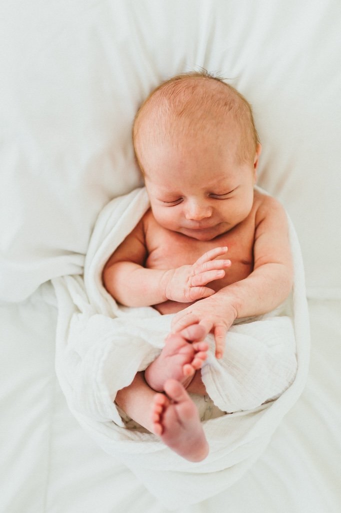Infant newborn laying on white sheets. 