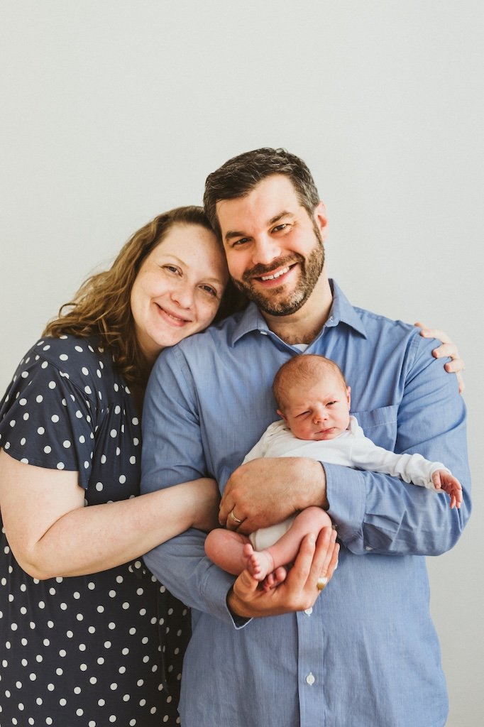 Parents smiling with newborn son in a photography studio.