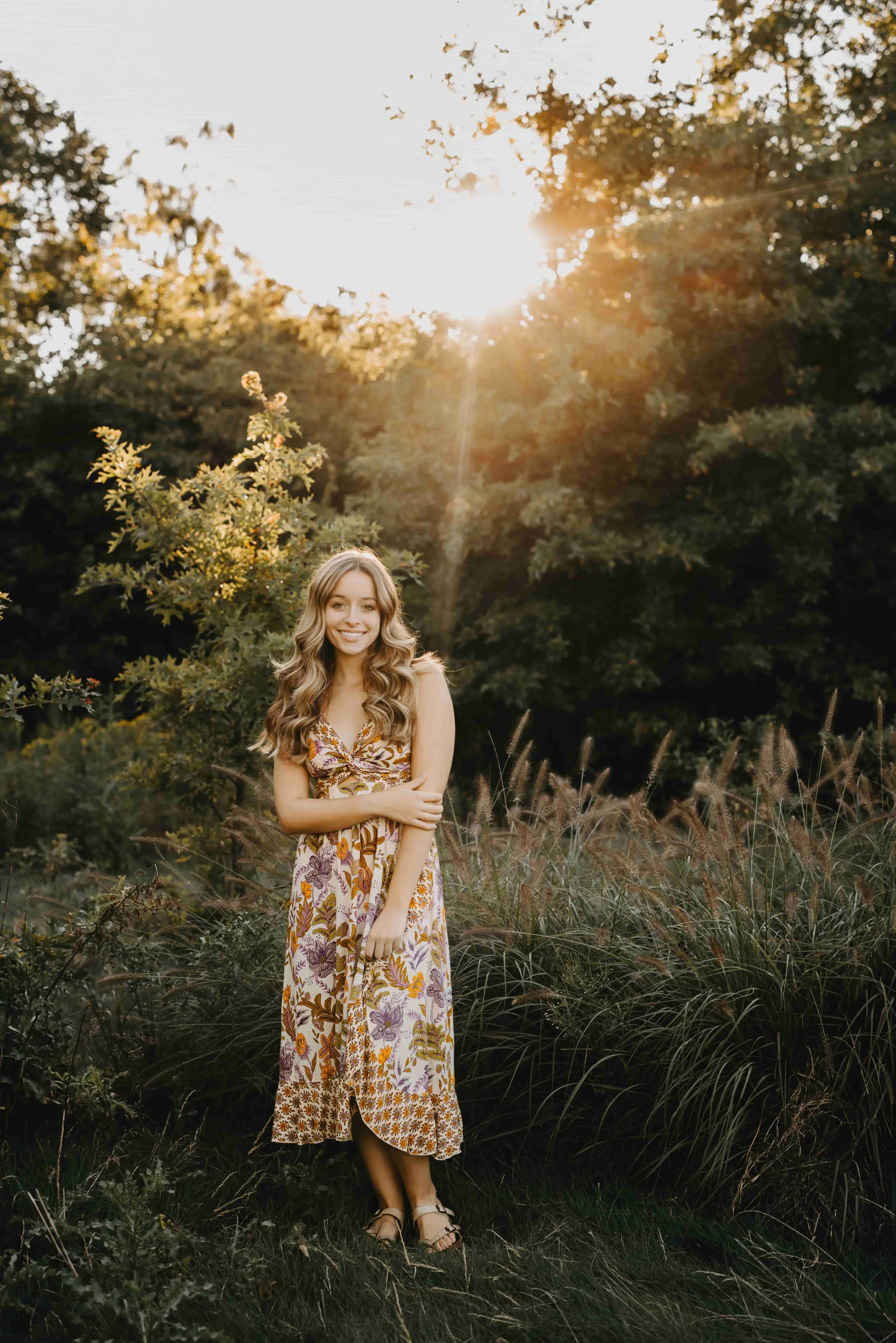 High school senior girl standing in tall grass at Acacia Reservation in Cleveland during golden hour, wearing a bohemian floral midi dress.