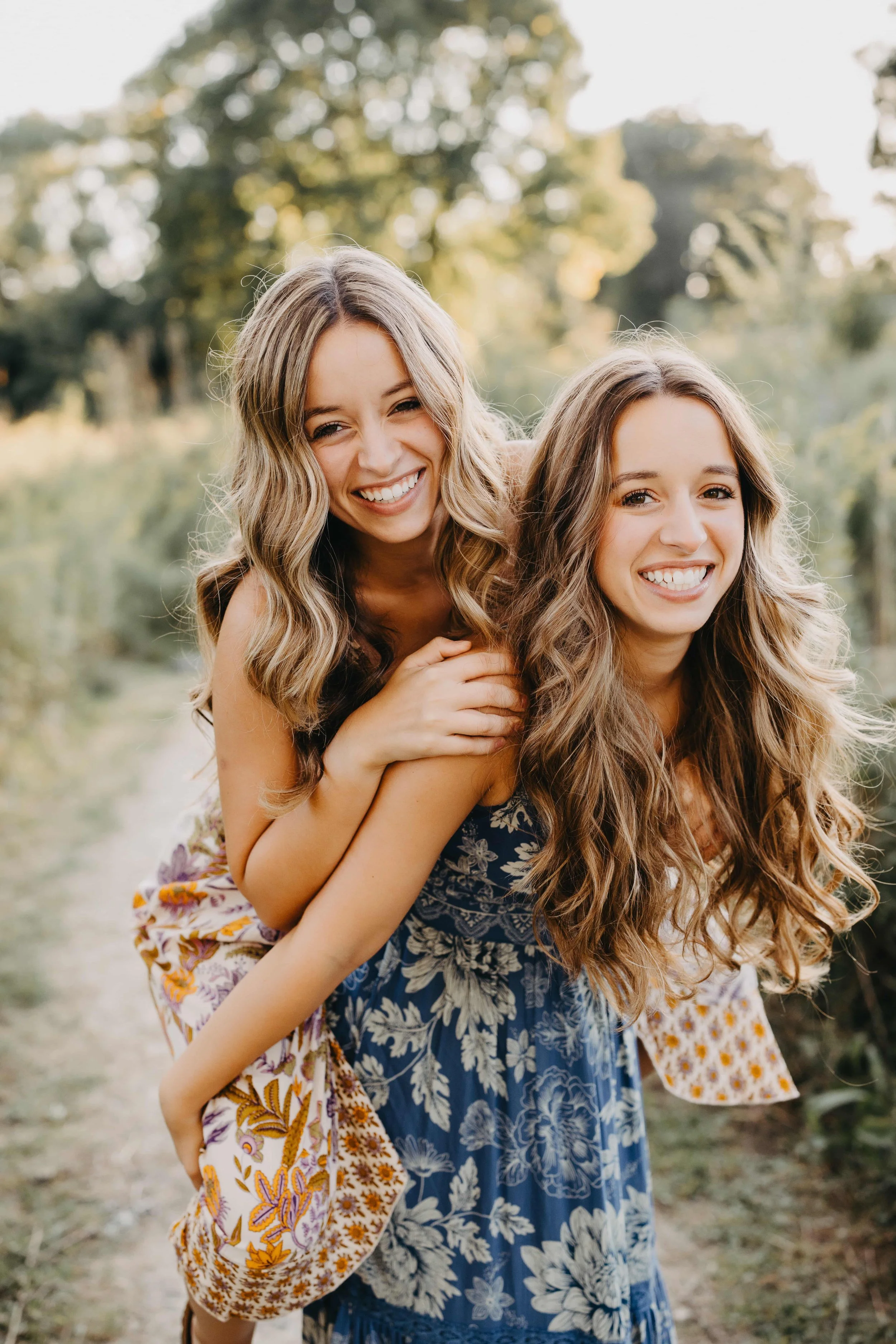 Twin sisters laughing together during a high school senior photo shoot in Cleveland, one wearing a floral yellow dress and the other a blue floral dress.