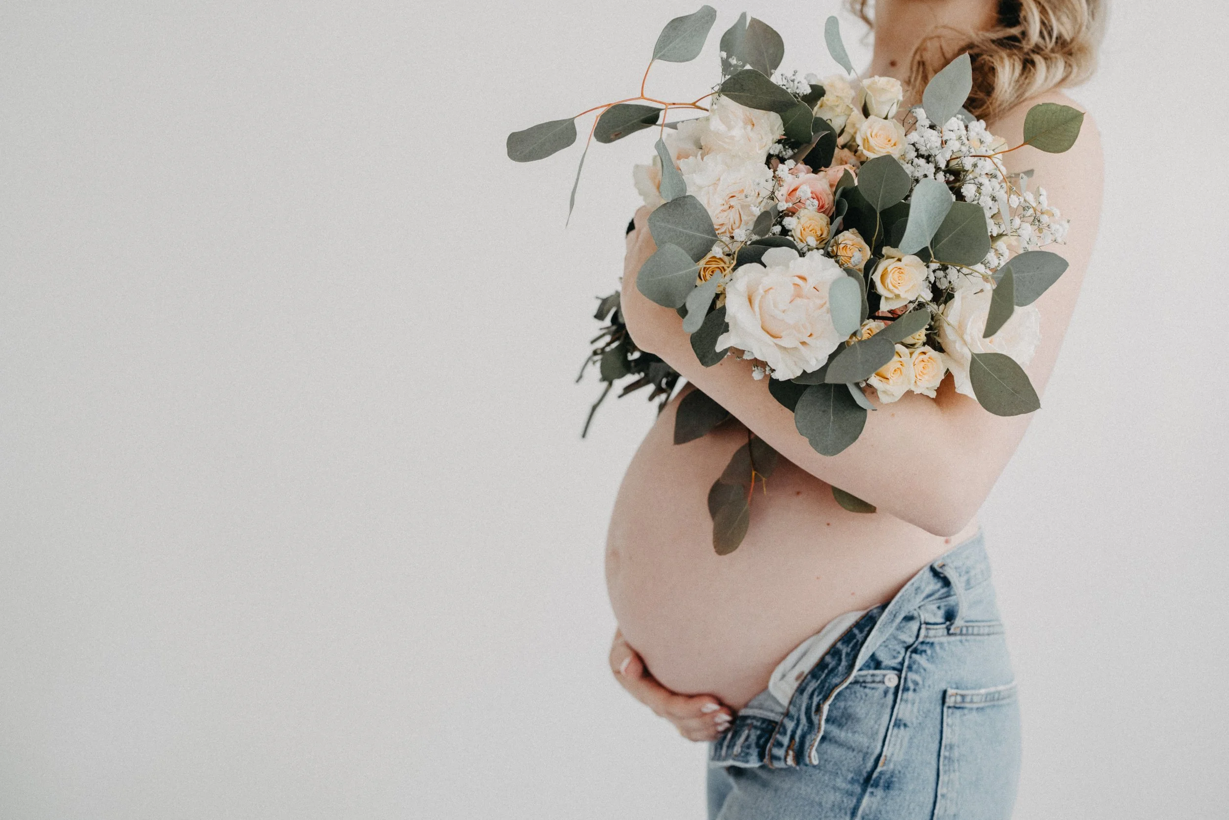 Pregnant woman wearing jeans with a floral bouquet during a studio maternity session in Cleveland.