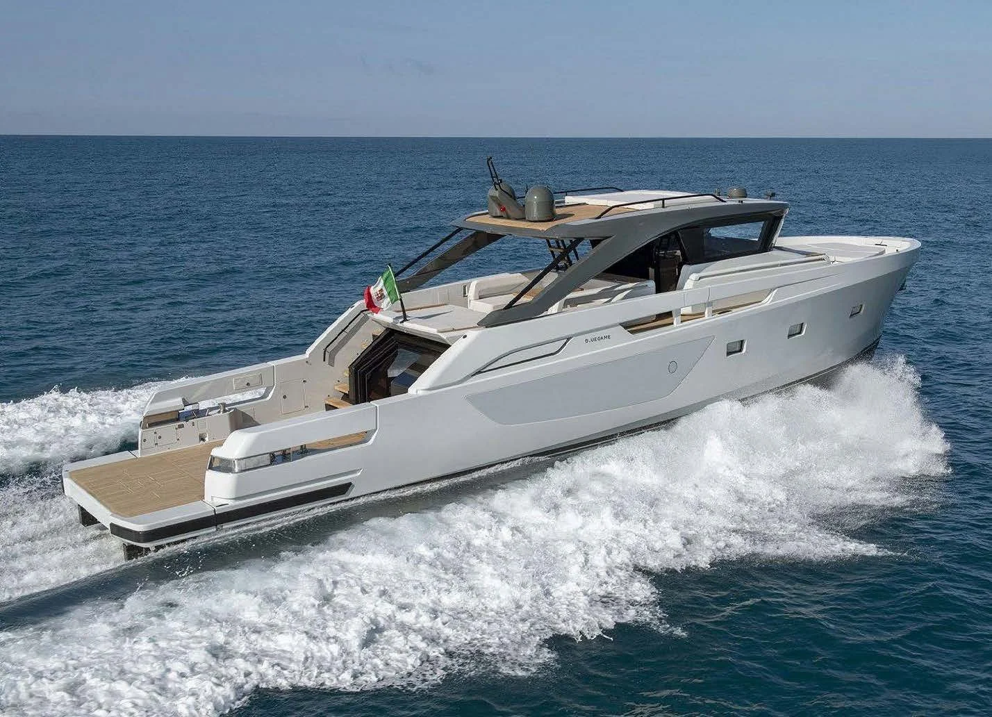 A sleek white yacht sailing on open water with a small Italian flag at the bow.