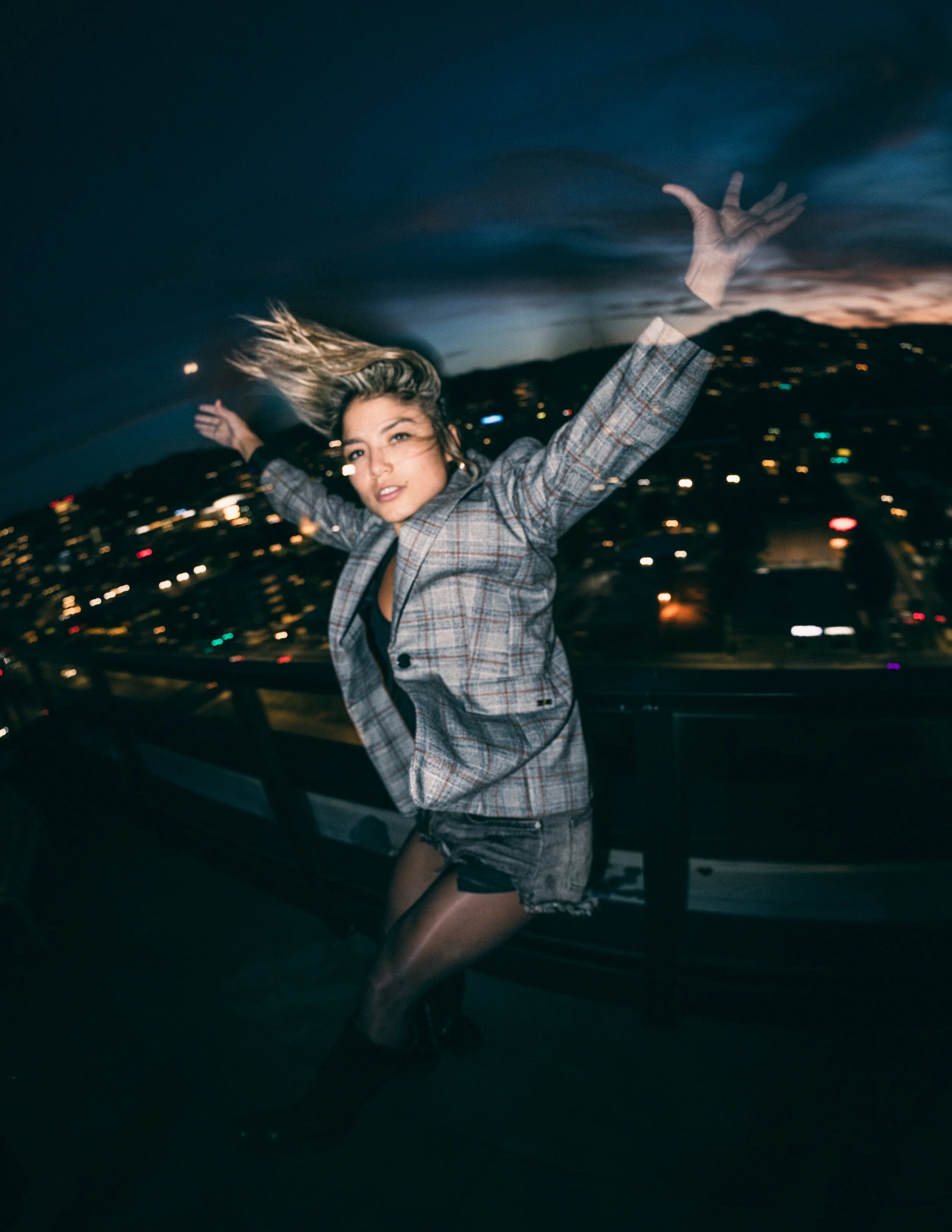 Model, Kim Gonzalez, on a PDX rooftop at sunset jumping with a Calvin Klein jacket and long exposure. Portland fashion photography by JP Bogan. Photo taken with with a Venus Optics Laowa 8-15mm f/2.8 Fisheye Lens and a Canon R5.