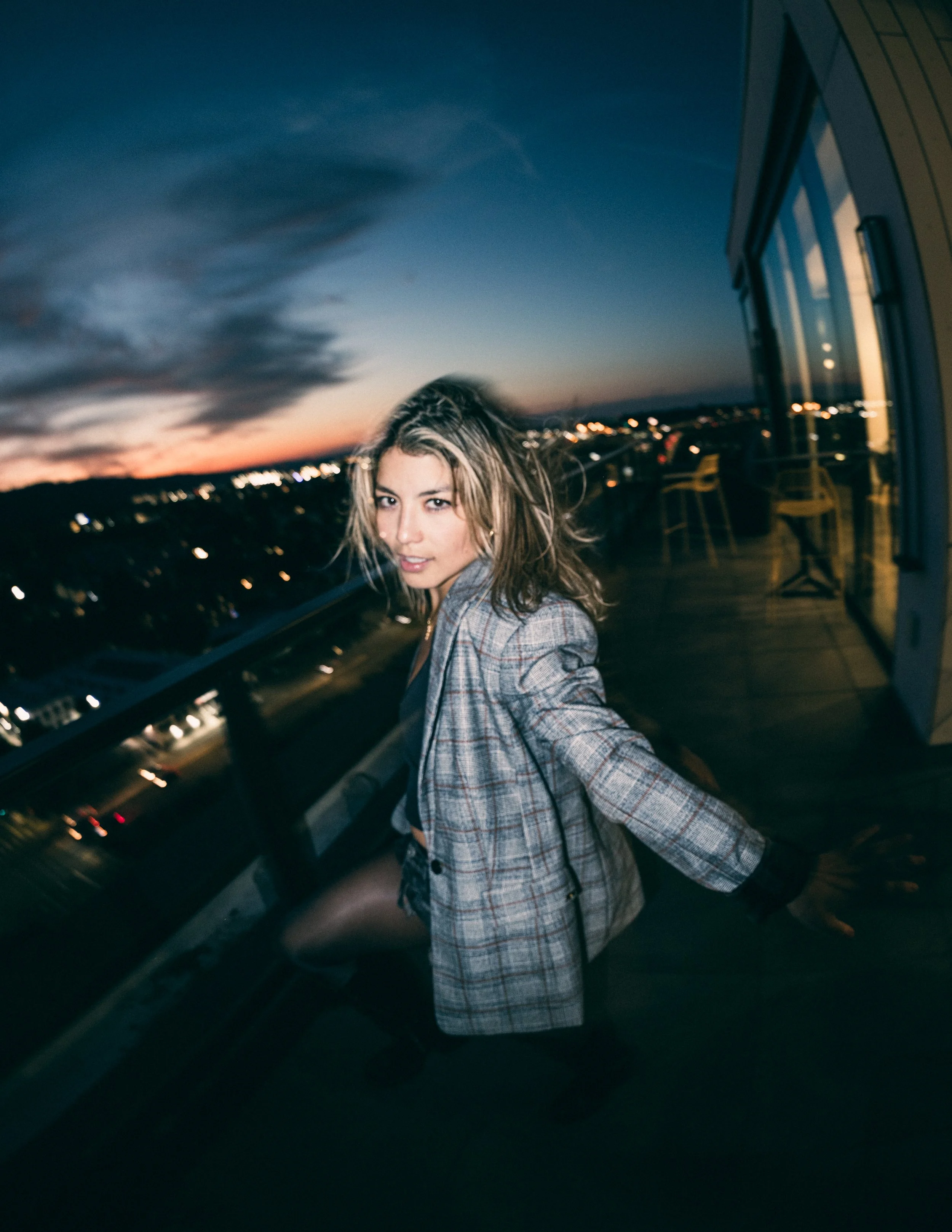Model, Kim Gonzalez, on a PDX rooftop at sunset posing with a Calvin Klein jacket and long exposure. Portland fashion photography by JP Bogan. Photo taken with with a Venus Optics Laowa 8-15mm f/2.8 Fisheye Lens and a Canon R5.