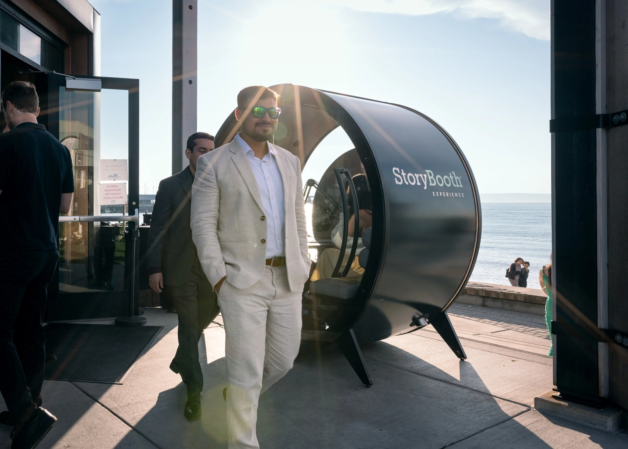 A man in a suit walking by a podcast booth with the sun in the background. Story Booth Experience product photography at a wedding in Seattle.