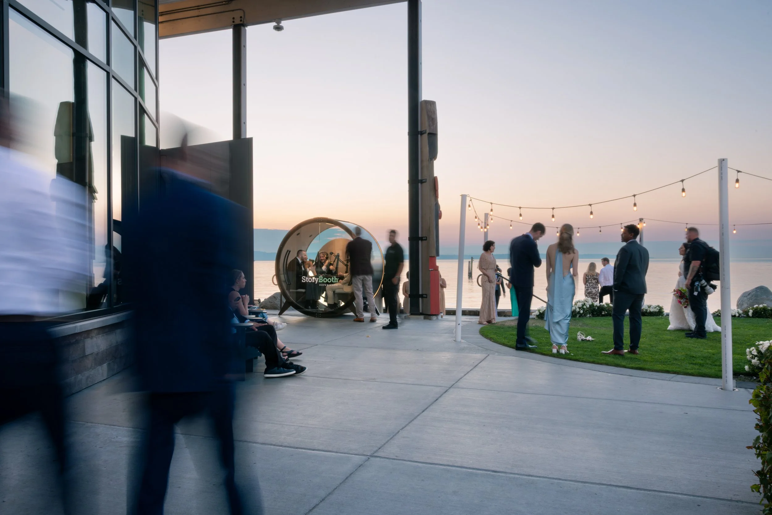 Wedding guests visiting and walking by a podcast booth. Story Booth Experience product photography at a wedding in Seattle.