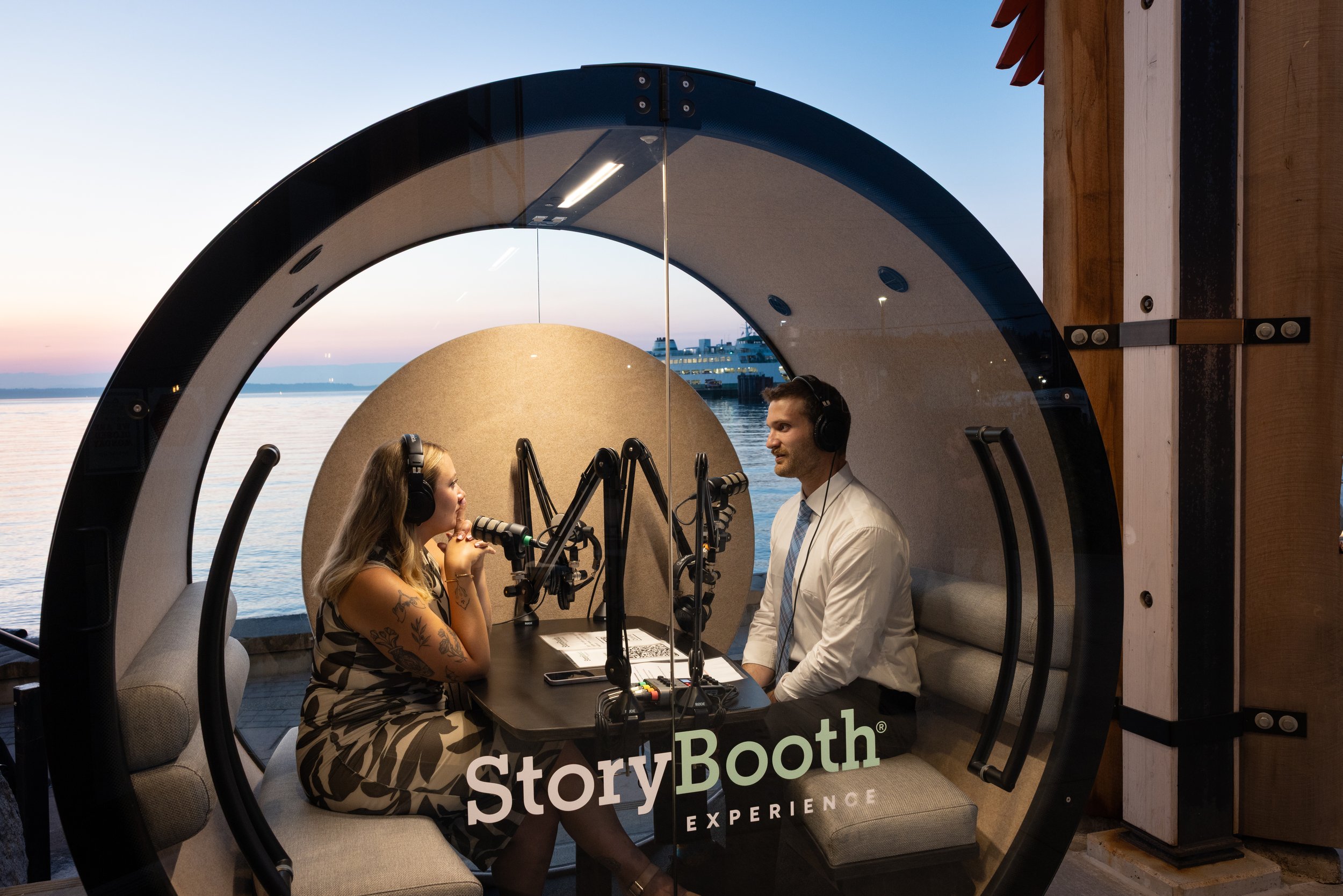 A couple inside a podcast booth with the ocean behind them. Story Booth Experience product photography at a wedding in Seattle.