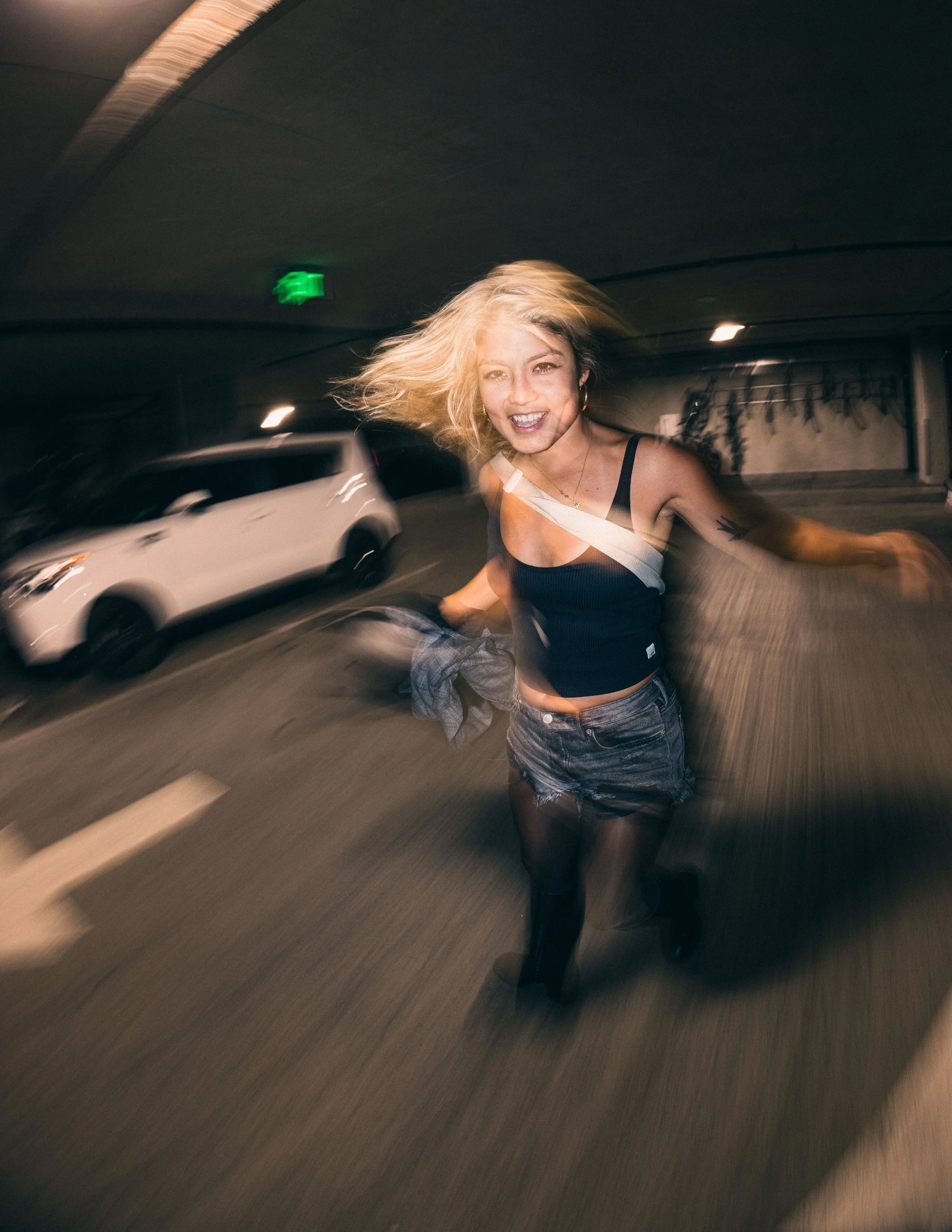 Model, Kim Gonzalez, on a PDX rooftop at sunset posing on a car with a Calvin Klein jacket and long exposure. Portland fashion photography by JP Bogan. Photo taken with with a Venus Optics Laowa 8-15mm f/2.8 Fisheye Lens and a Canon R5.