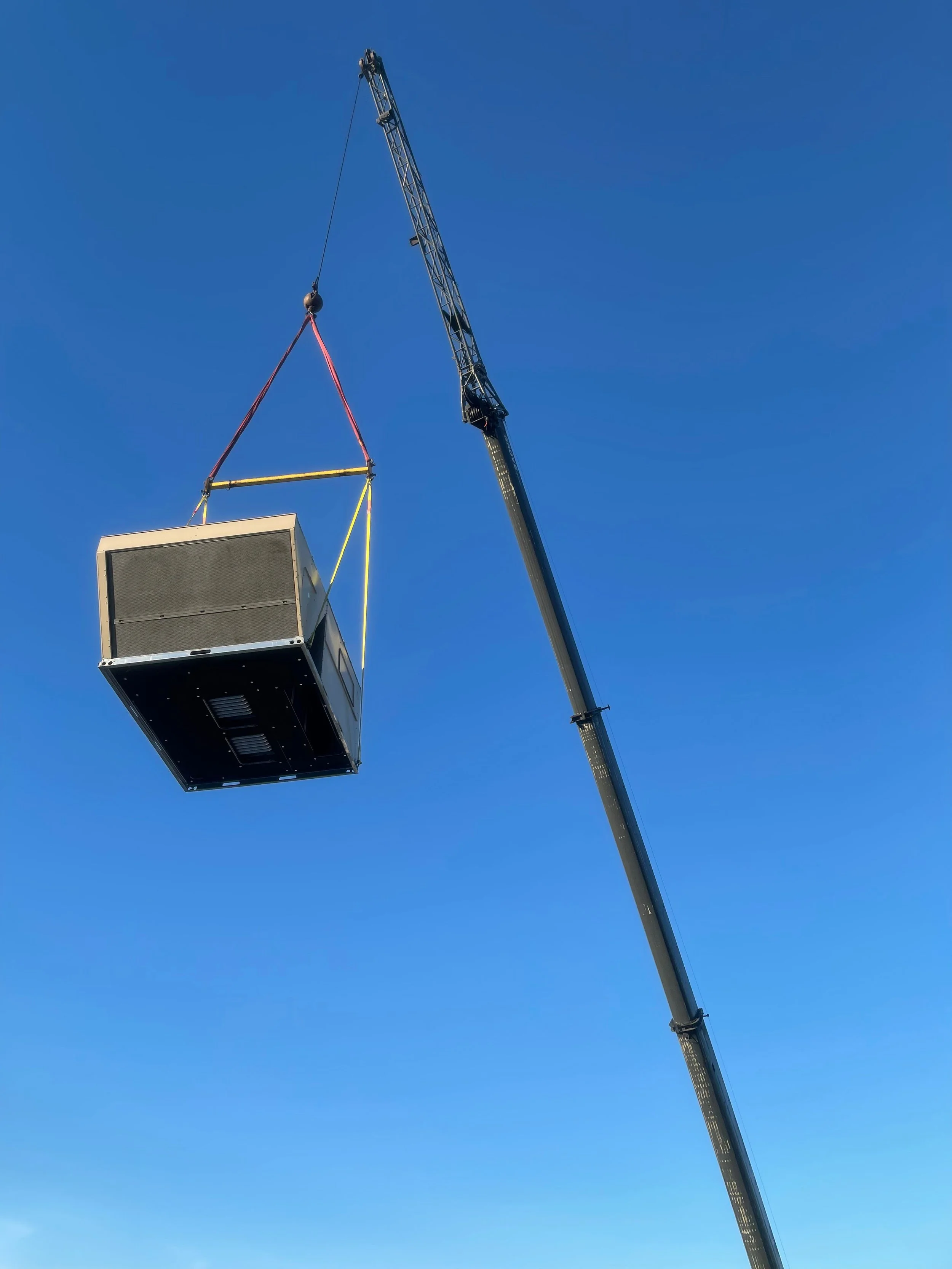 Crane lifting a commercial rooftop HVAC unit onto a building