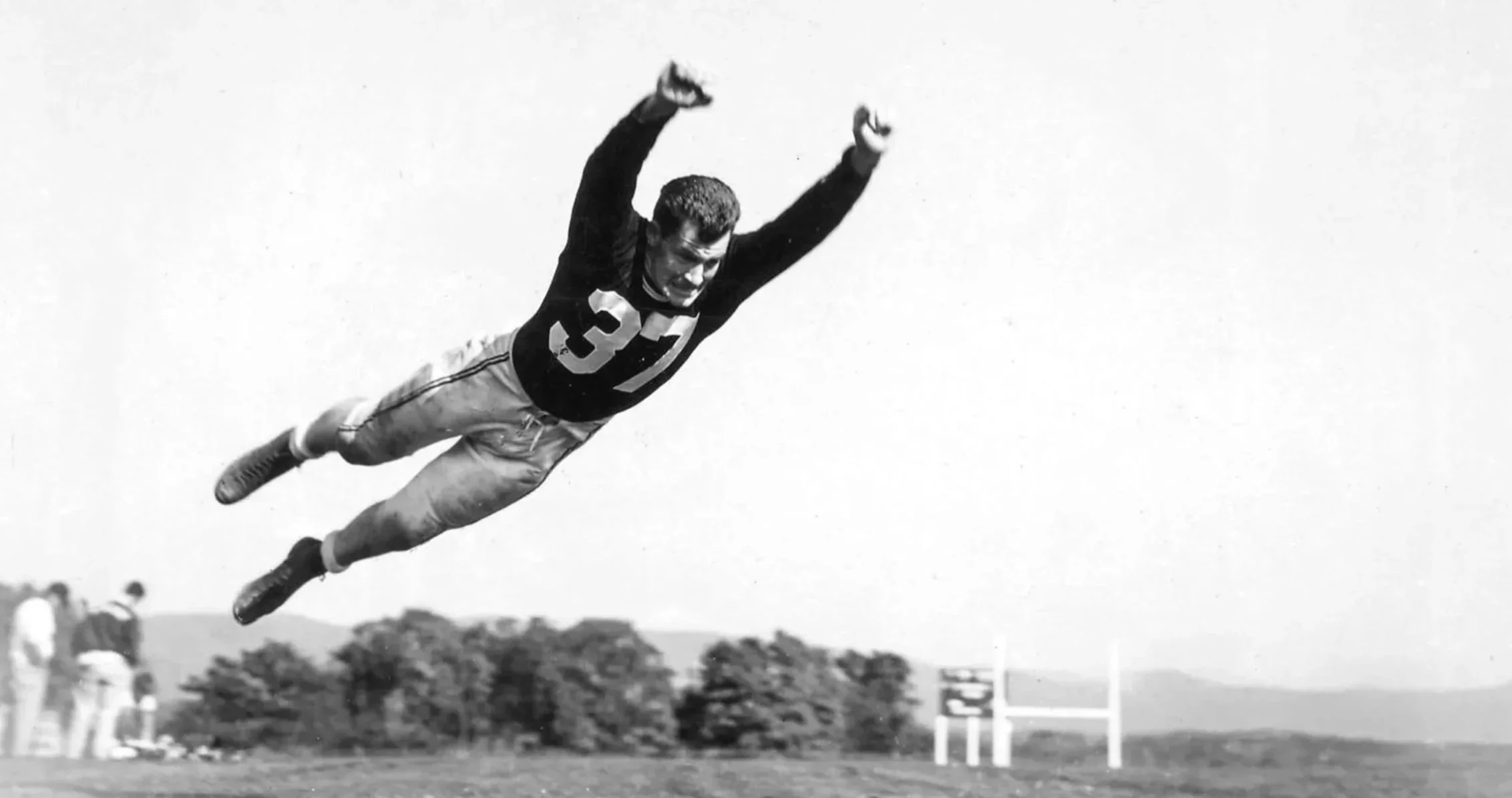 Vintage black‑and‑white photo of a football player wearing jersey 37 diving mid‑air across a grassy field, capturing athletic motion, grit, and timeless field‑day energy.