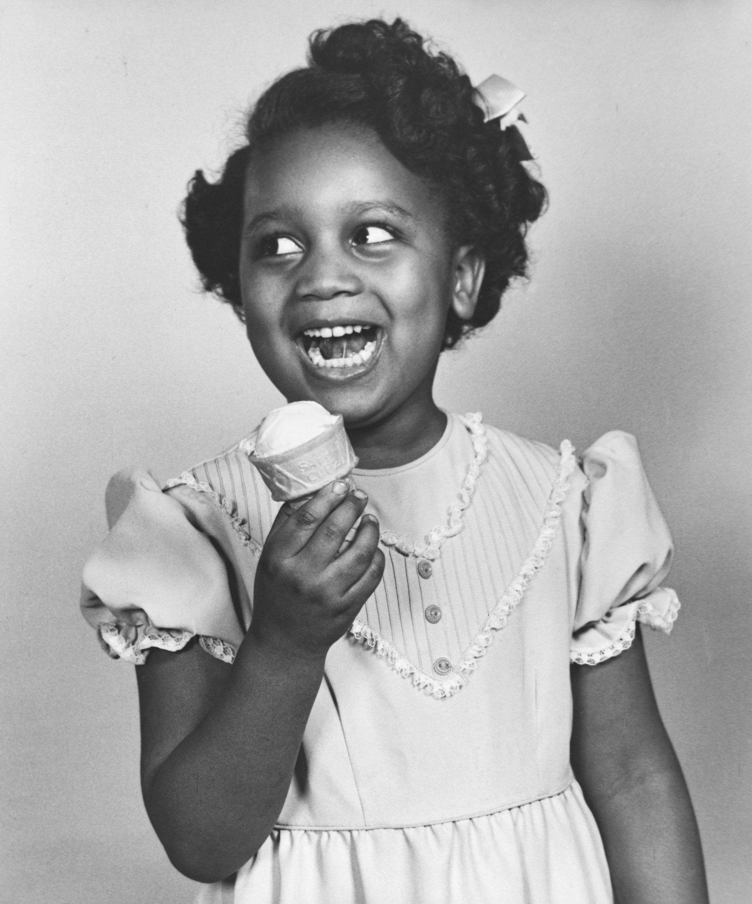 Black‑and‑white portrait of a young girl smiling brightly while holding an ice cream cone, capturing joy, innocence, and the playful, heartfelt energy that inspires Field Day’s design ethos.
