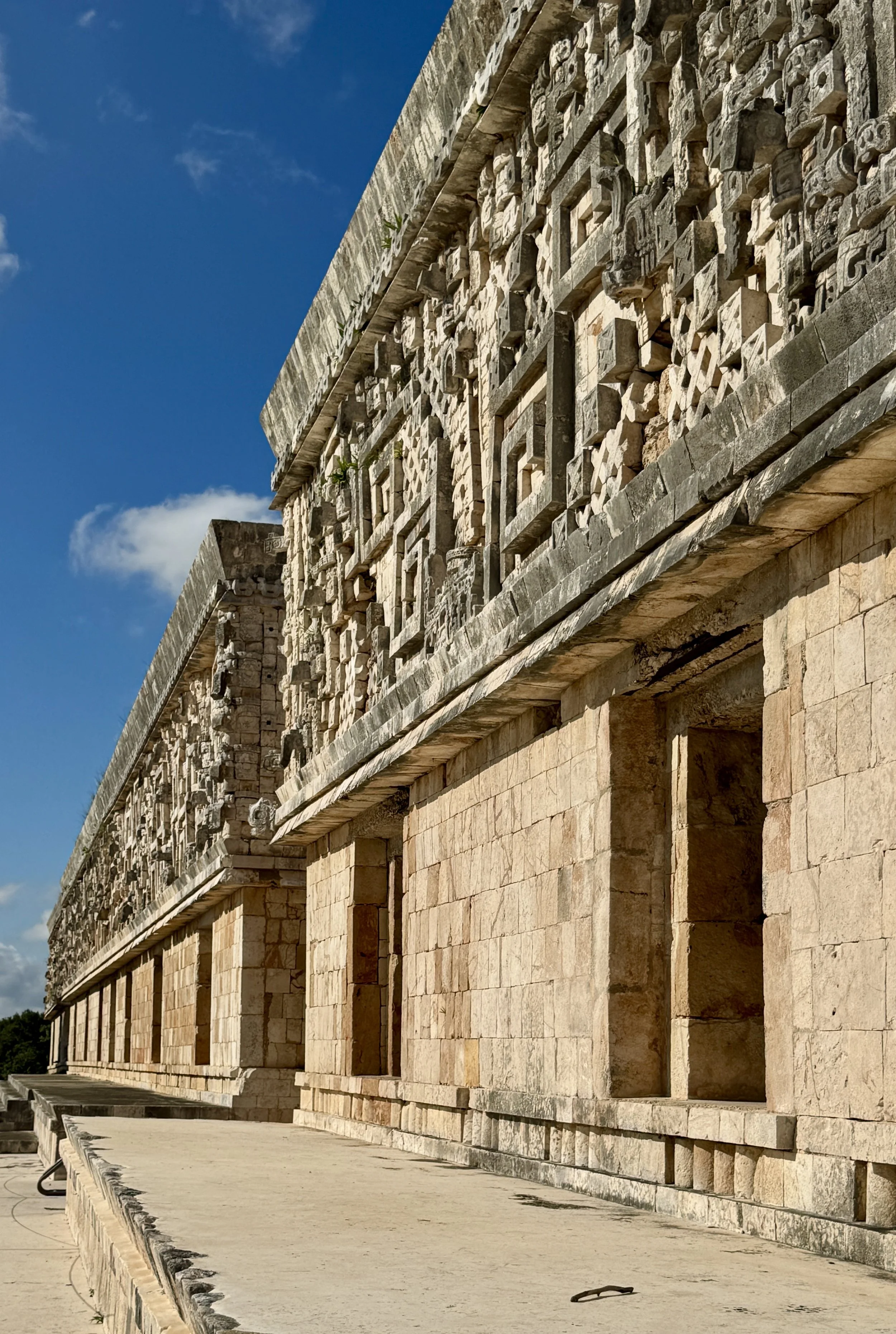Close-up of an ancient Maya stone temple with carved stone reliefs, set against a bright blue sky in Uxmal, Yucatan, Mexico.