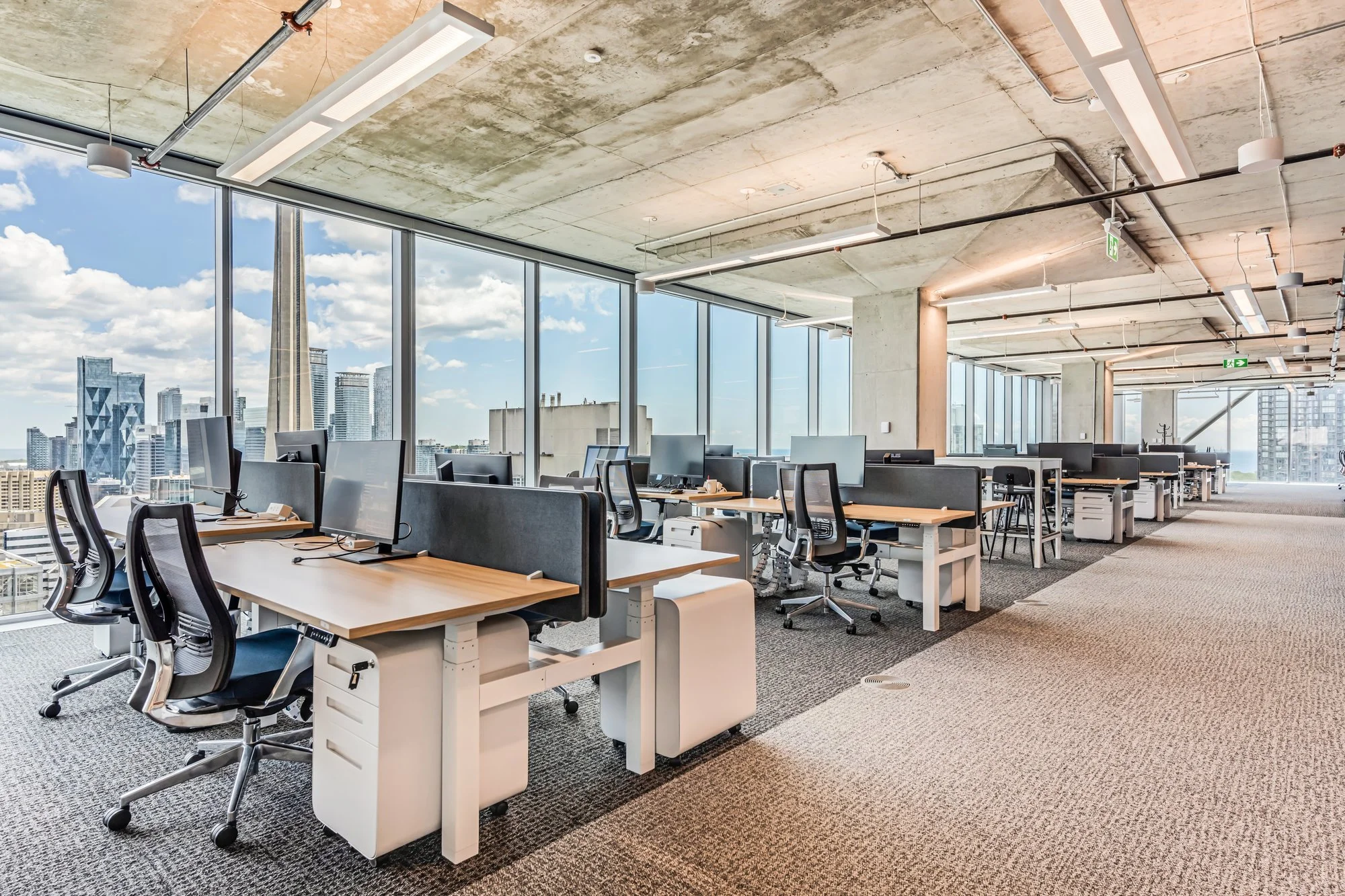 Modern open office space with workstations, ergonomic chairs, and large windows offering a city skyline view.