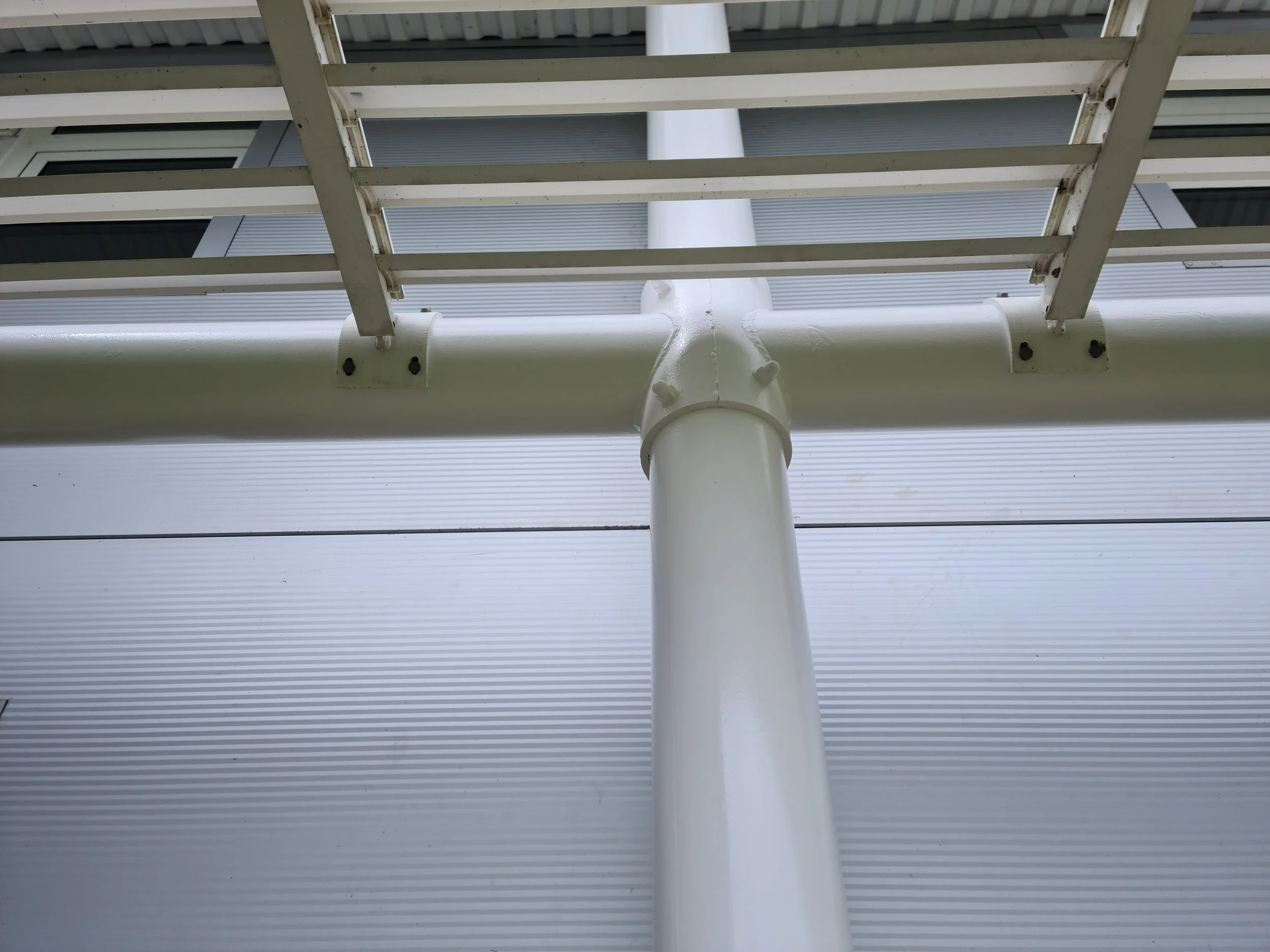 Looking up at a white metal gutter and downspout on the side of a building, with part of a white ladder in the foreground.