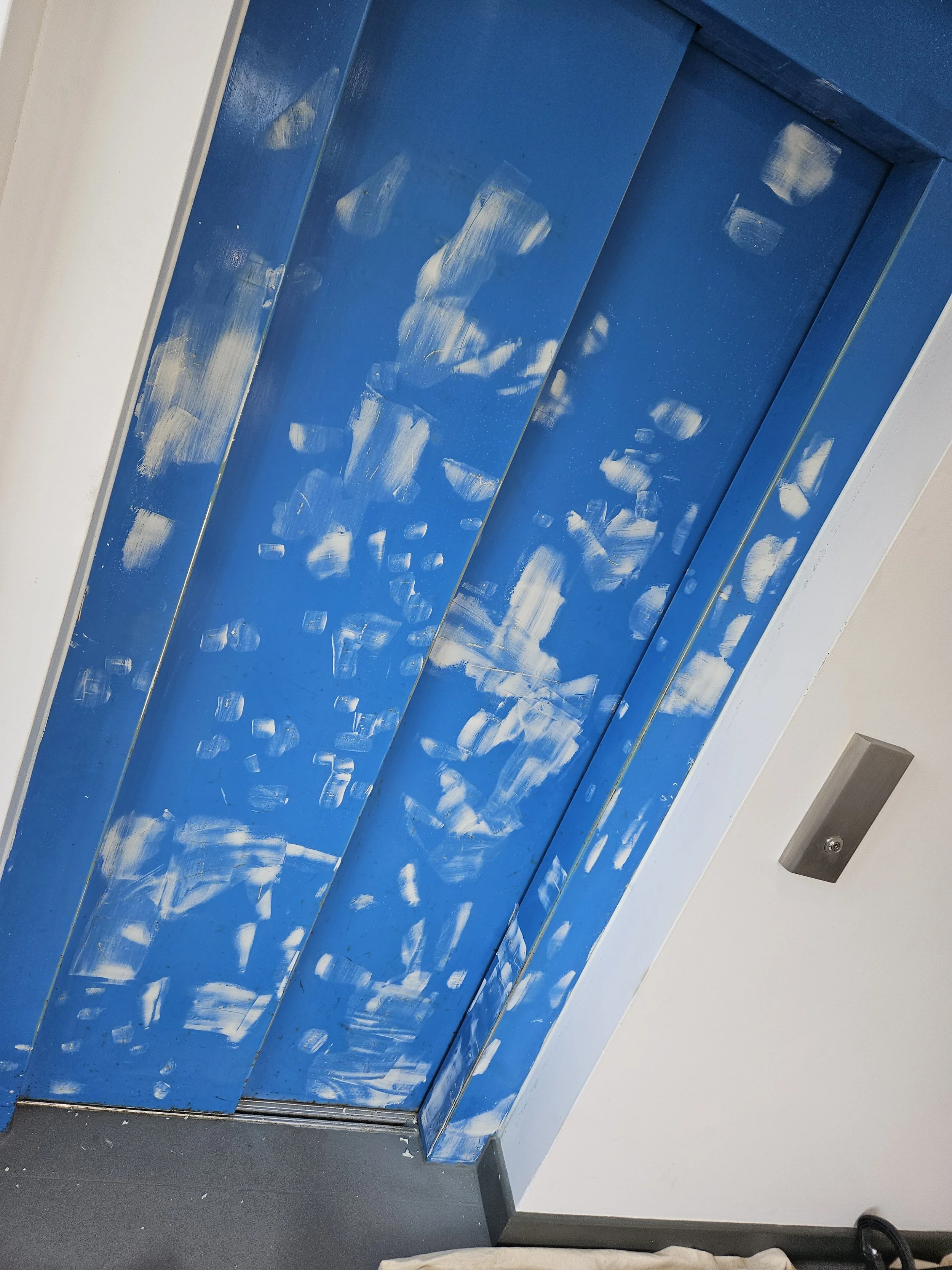 Blue elevator door with white paint or chalk marks on it in an interior space.