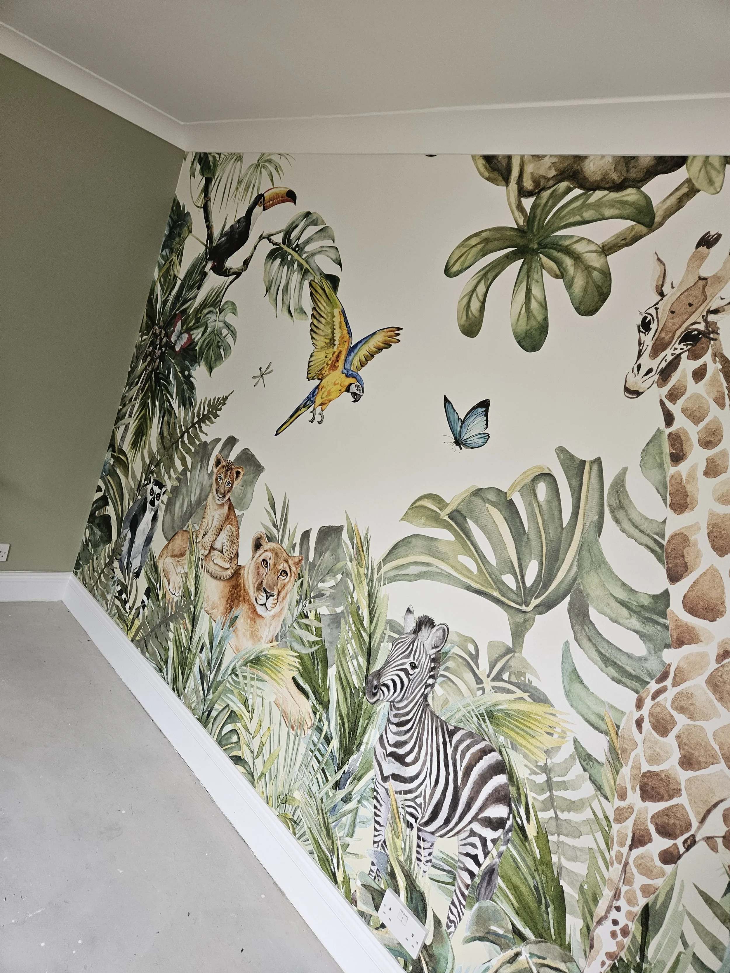 Murals of animals including giraffe, zebra, lion, lemur, toucan, parrot, butterfly, and lush green tropical leaves on a corner wall.