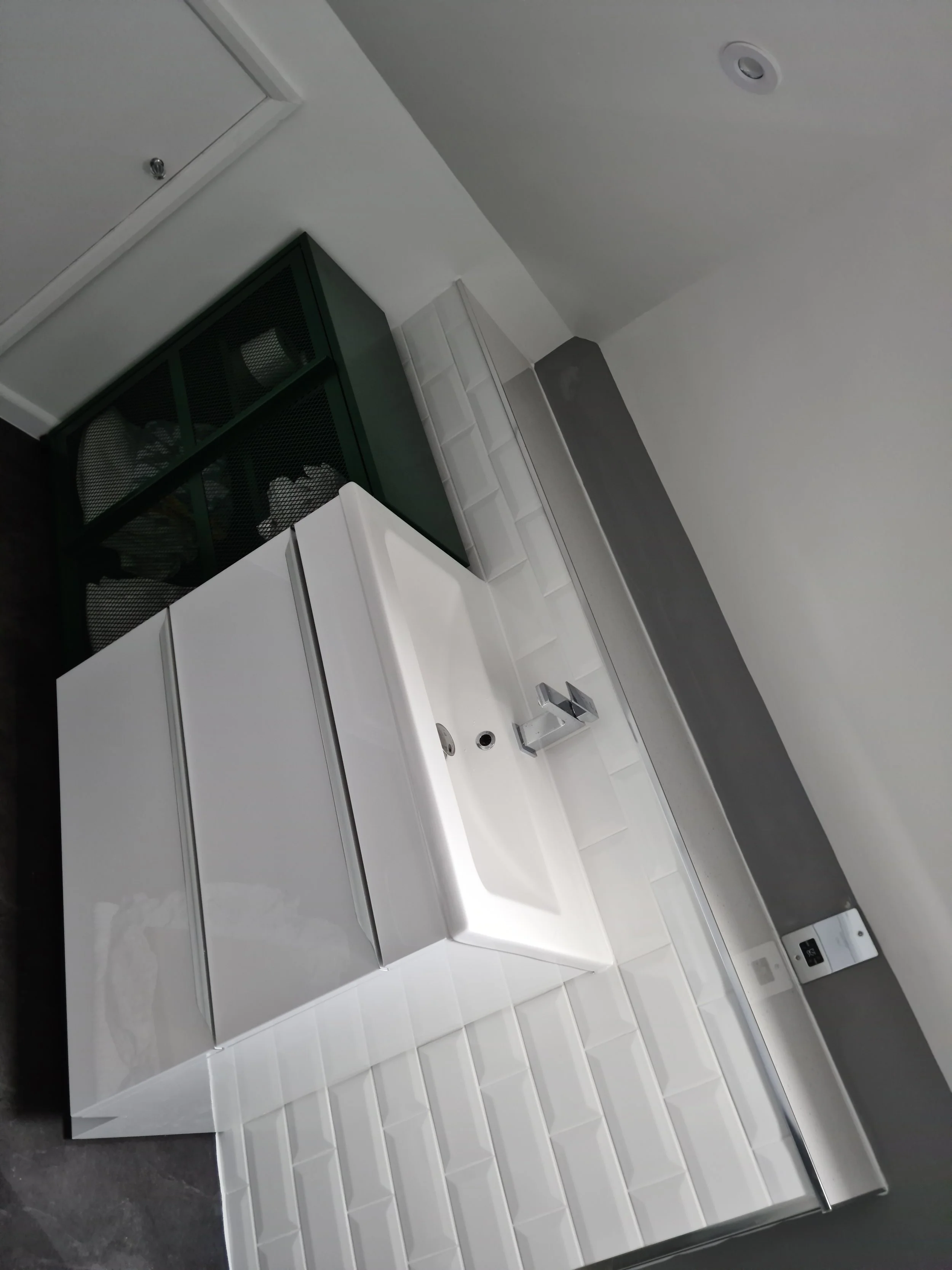 Modern white vanity with built-in sink and chrome faucet, against a tiled wall, with a gray wall and electrical outlet nearby.