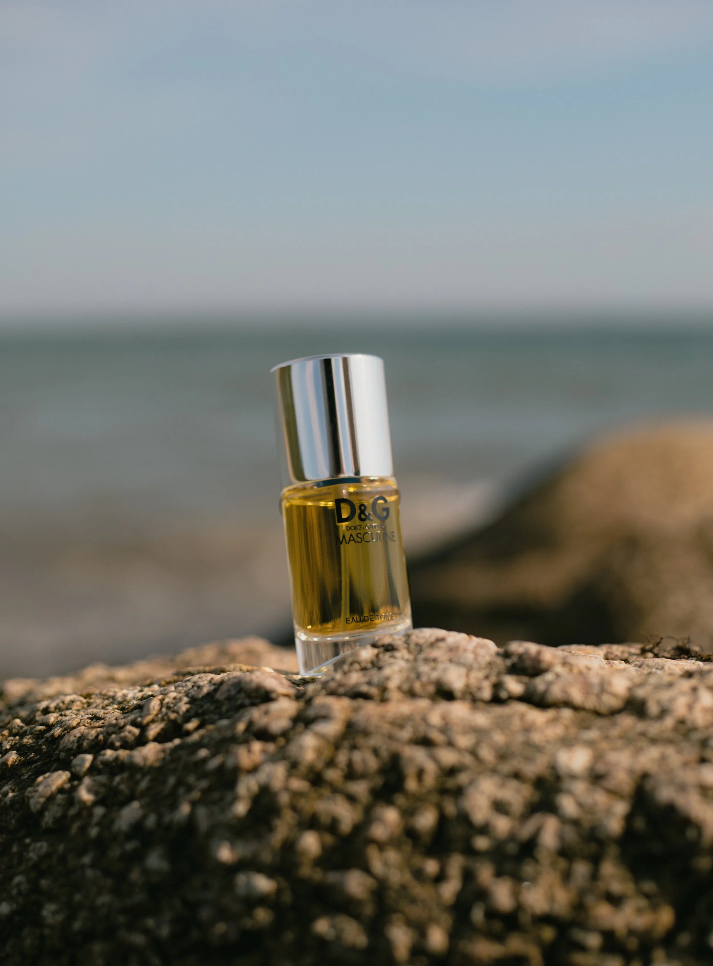En flaske D&G Dolce & Gabbana parfume står på en klippe ved havet.