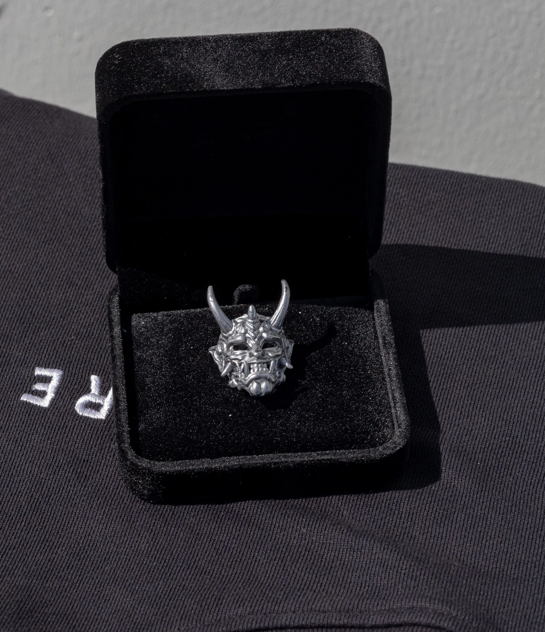 En sølvfarvet ring med et frygtindgydende dragehoved design, placeret i en sort velouræske.