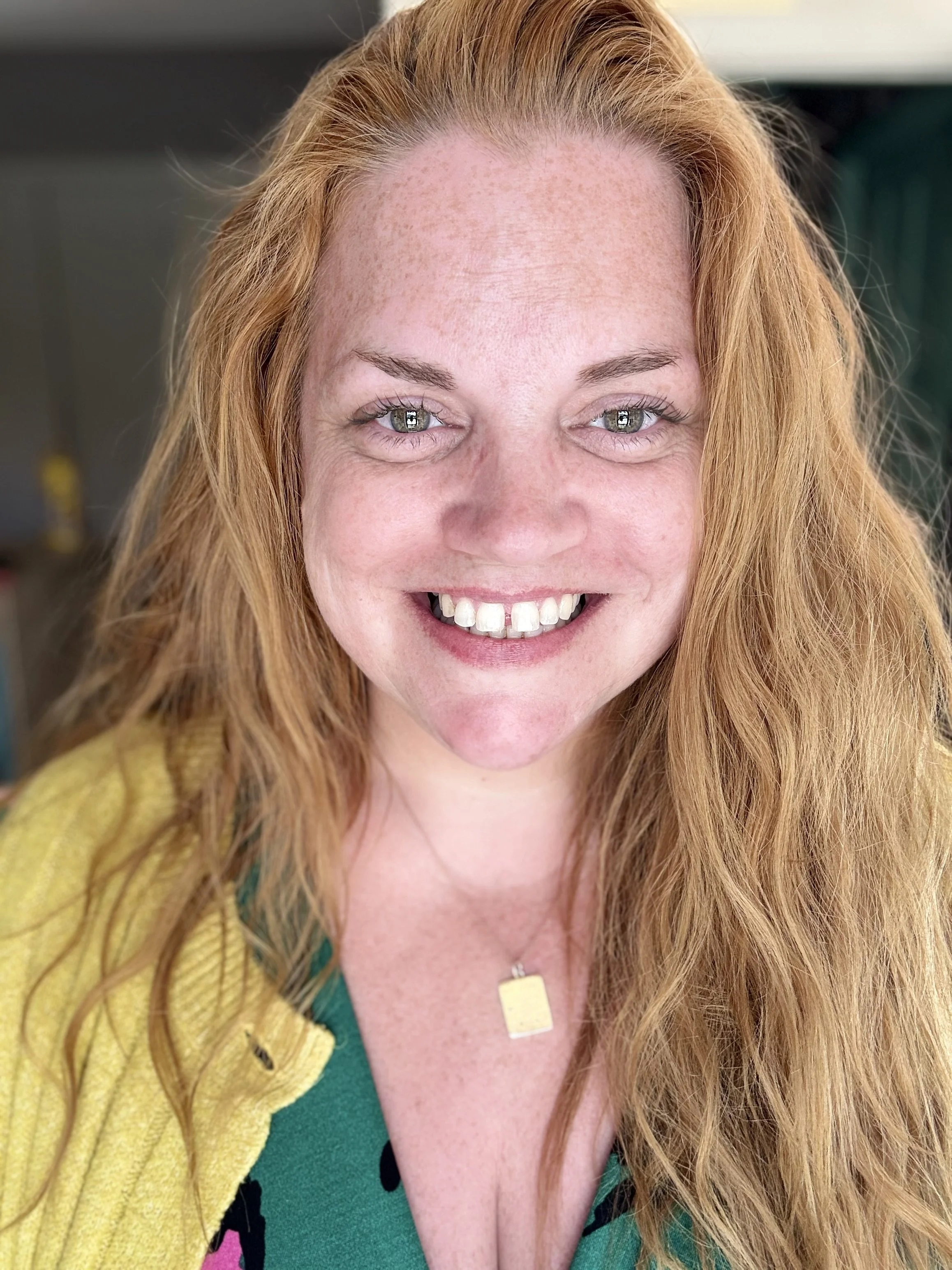 Smiling woman with red hair wearing colourful clothing in natural light