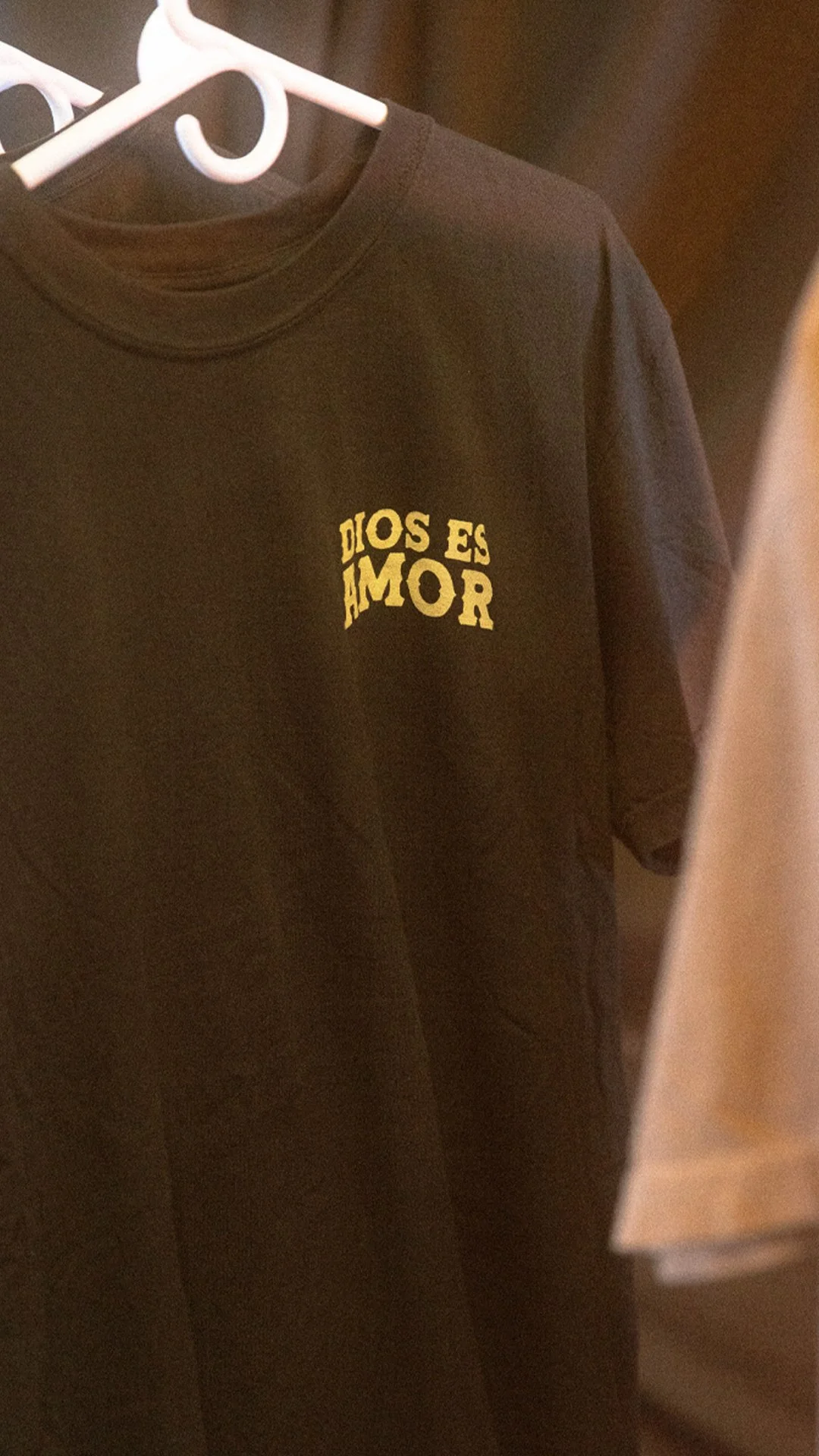 Black T-shirt with yellow text on the left chest area and hanging on a white plastic hanger.