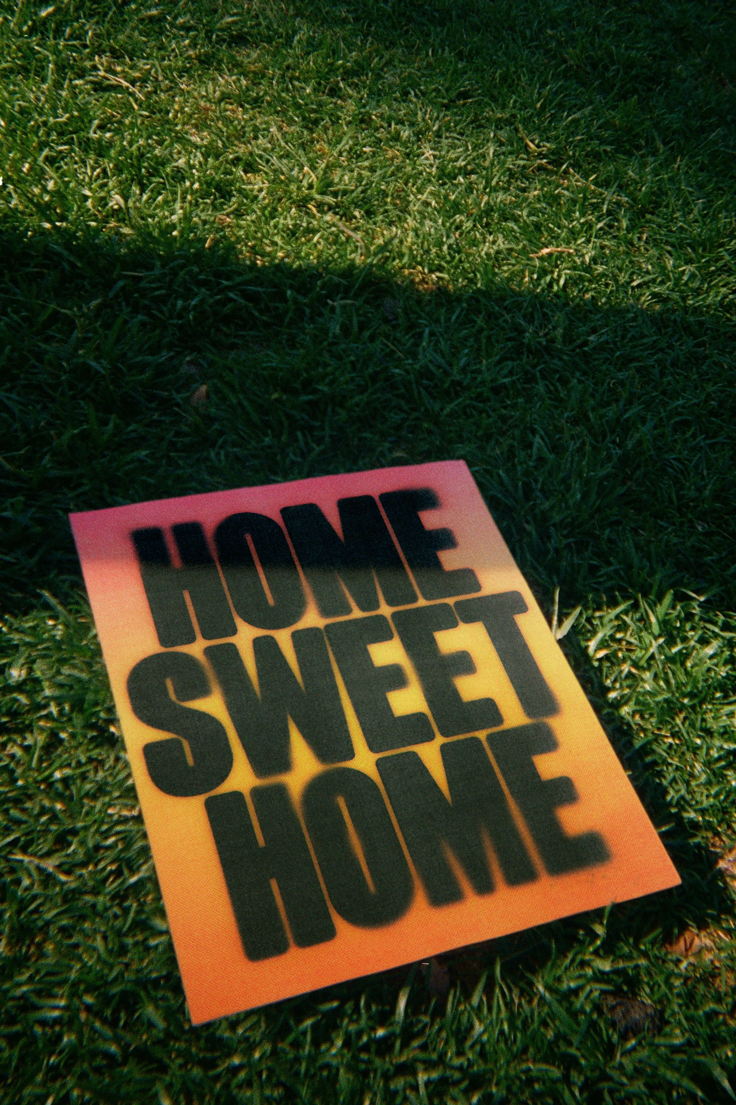 A sign with the words 'HONEY SWEET' in large black letters on a gradient background from yellow to orange, lying on green grass.