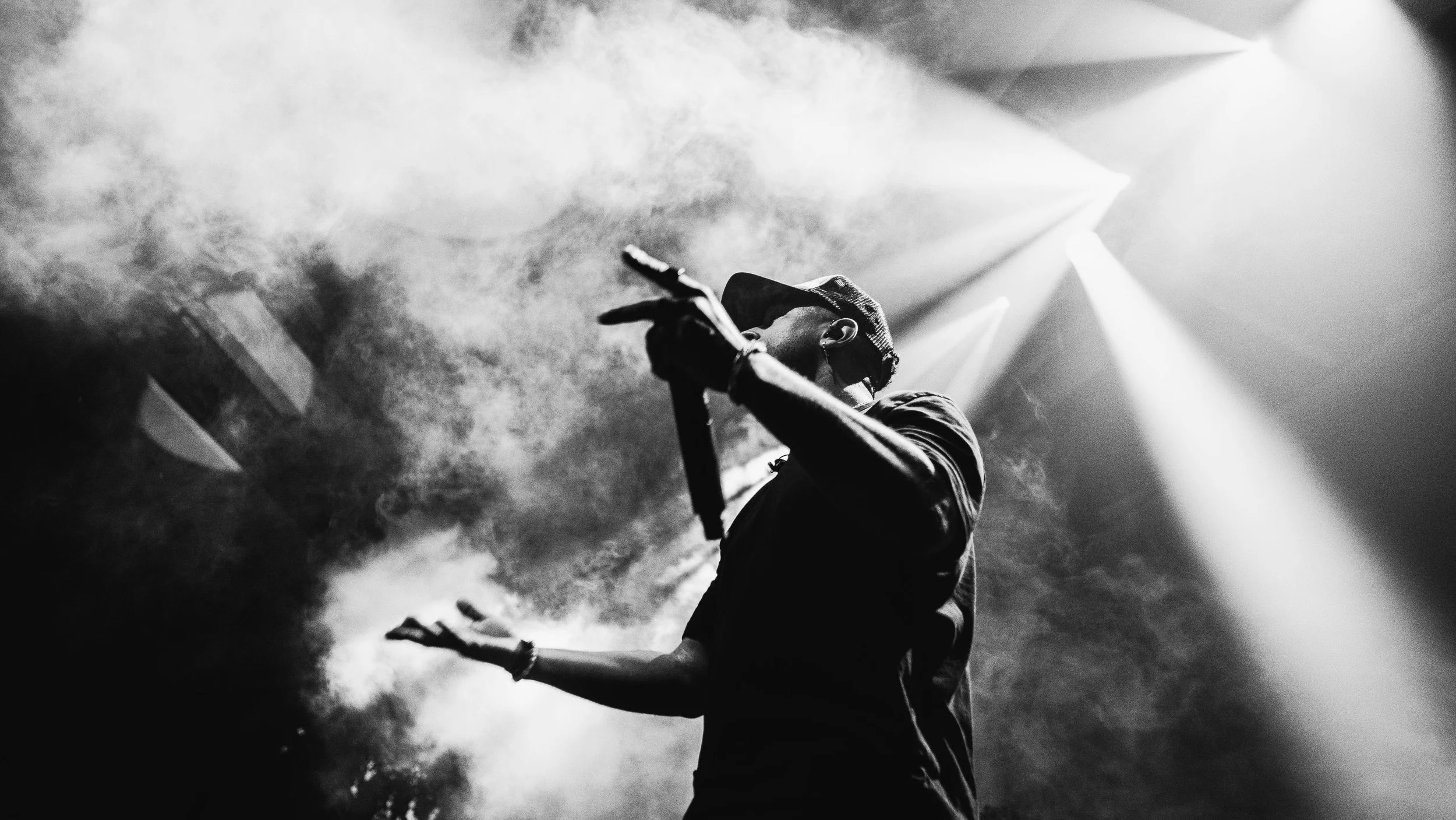 A person performing on stage with dramatic lighting and smoke, viewed from below in black and white.