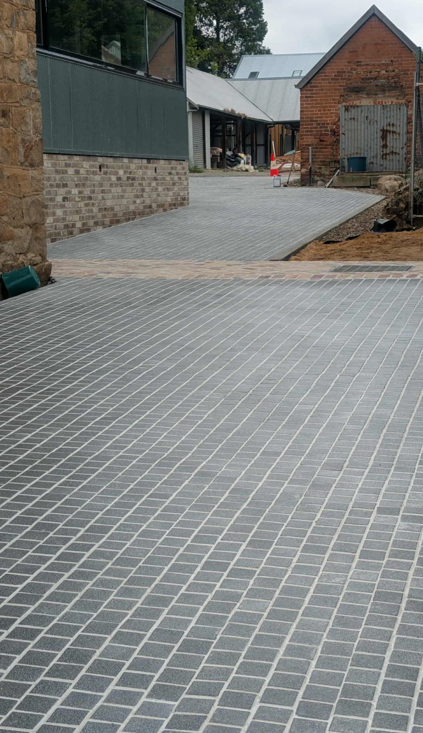 Newly paved brick driveway in front of a house with a brick and stone exterior, construction tools, and orange traffic cone.