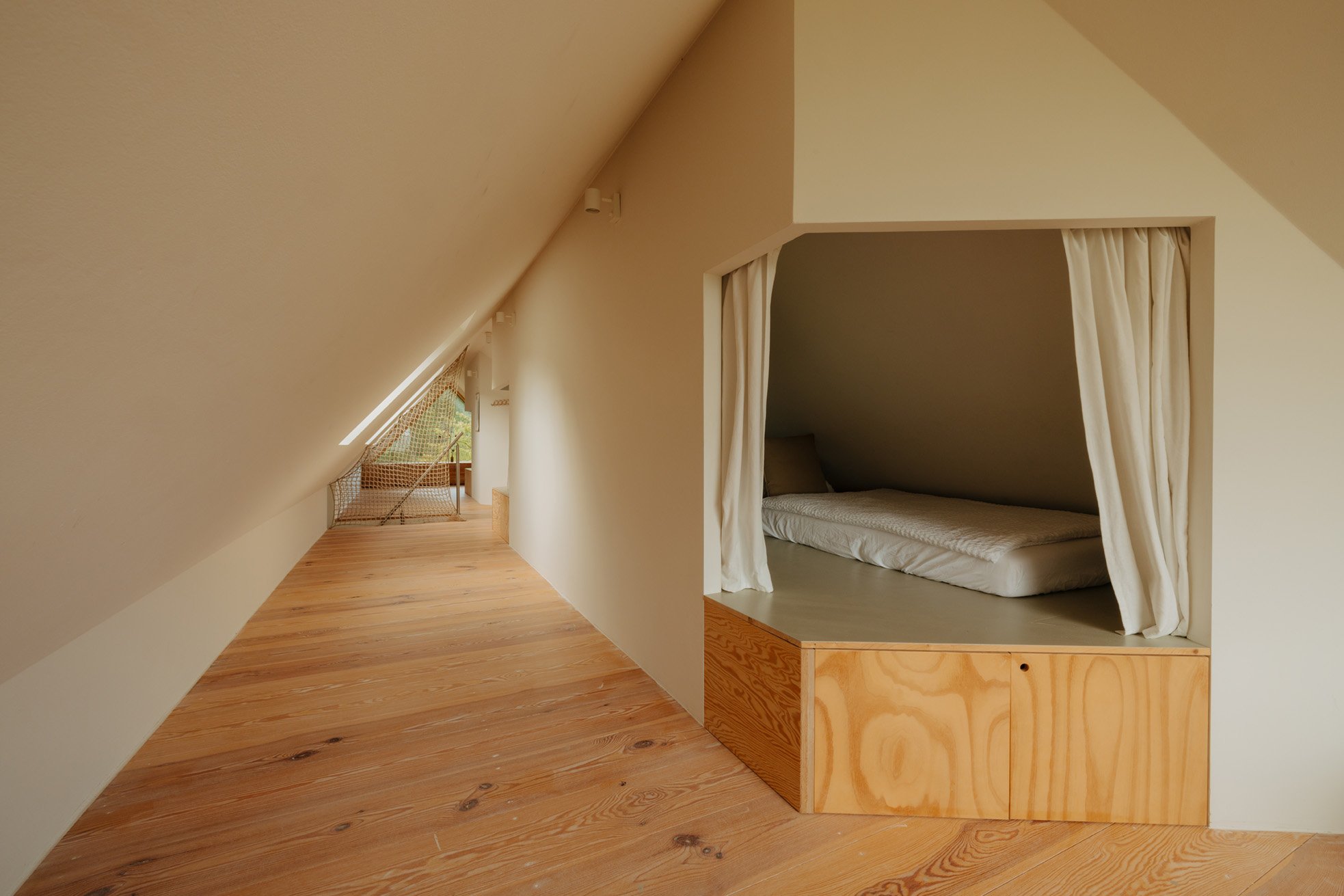 Small built-in bed with curtains on the right side of a cozy attic space, with sloped ceiling and wooden flooring.