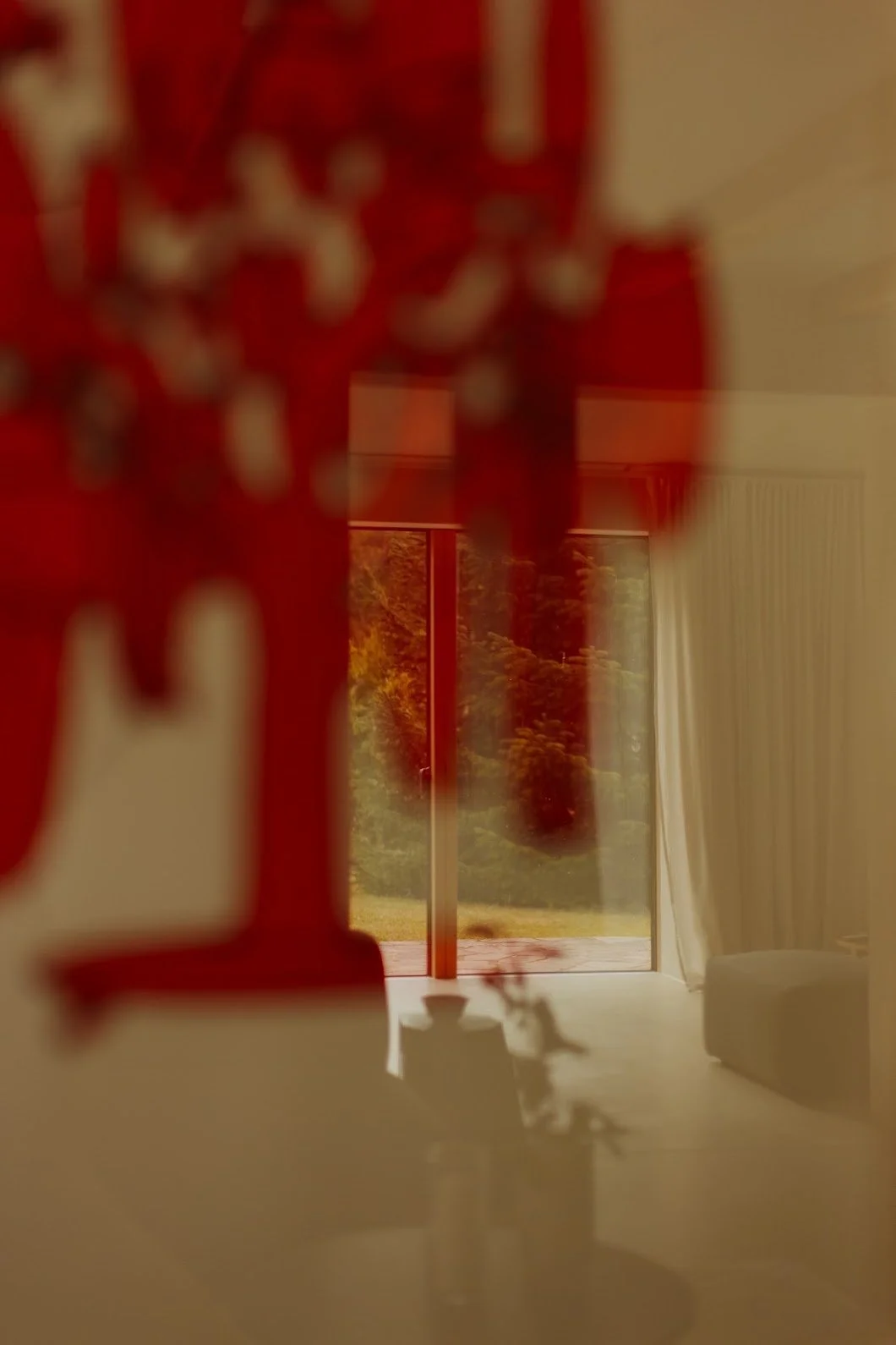 Mellenau 9. A blurred view of an indoor scene with a window showing trees outside, a white curtain, and floral decoration in the foreground.