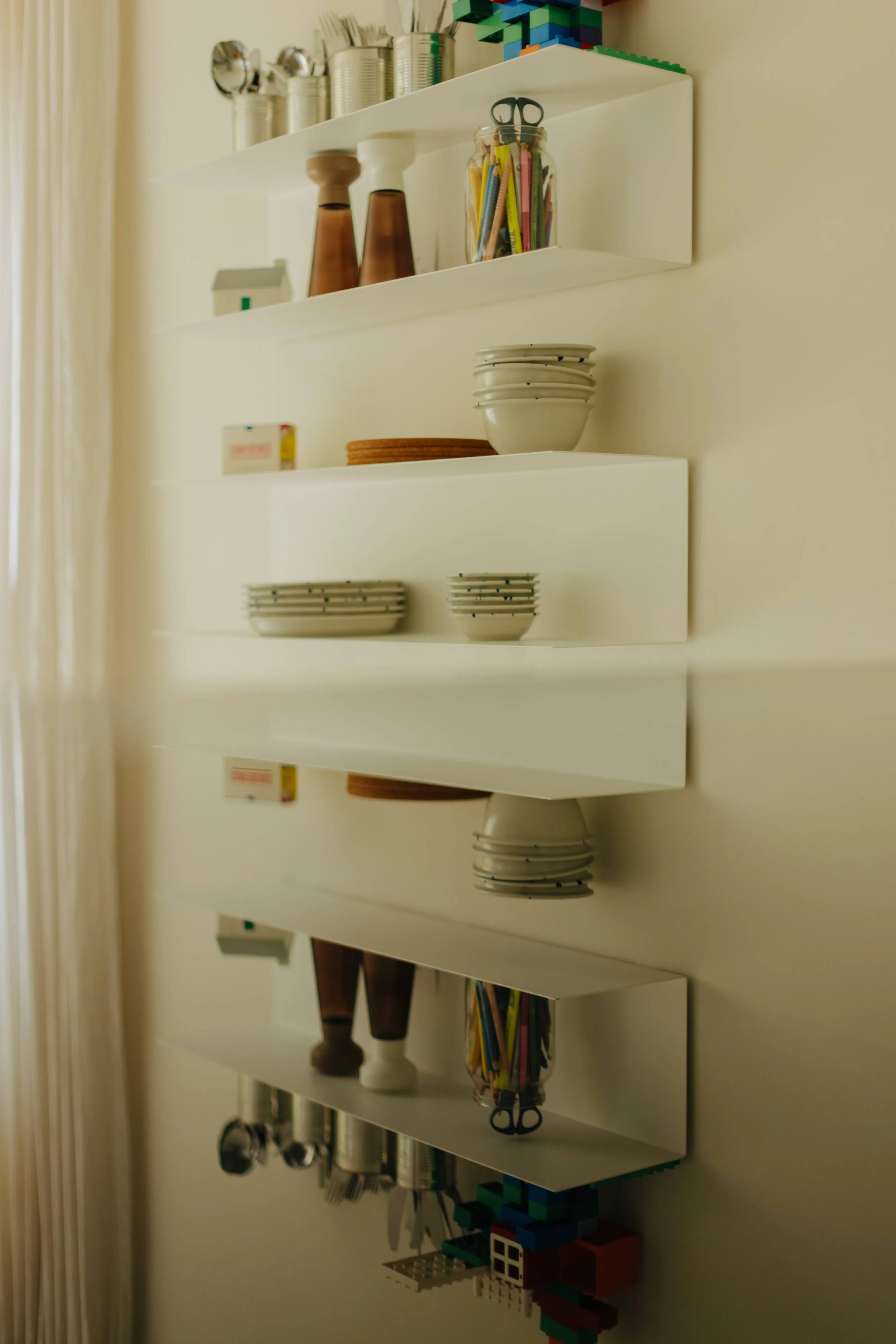Wall-mounted white shelves holding bowls, small jars, and kitchen utensils in a cozy kitchen.